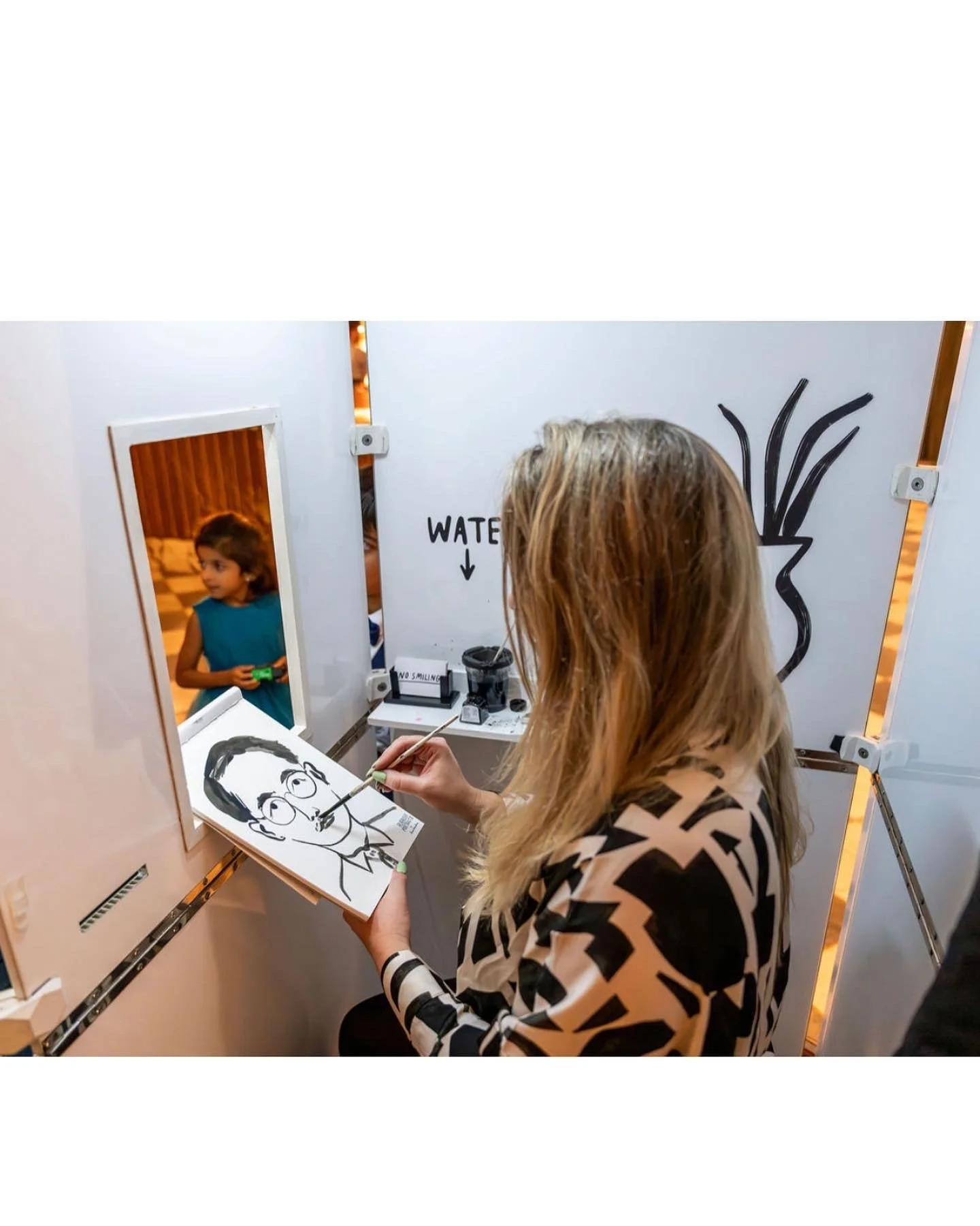 Lucie Sheridan paints a quick, characterful portrait inside the Rubbish Portraits live portrait booth as a young guest looks on in fascination. This quirky and creative feature offers guests a fun, interactive experience, resulting in a hand-painted 