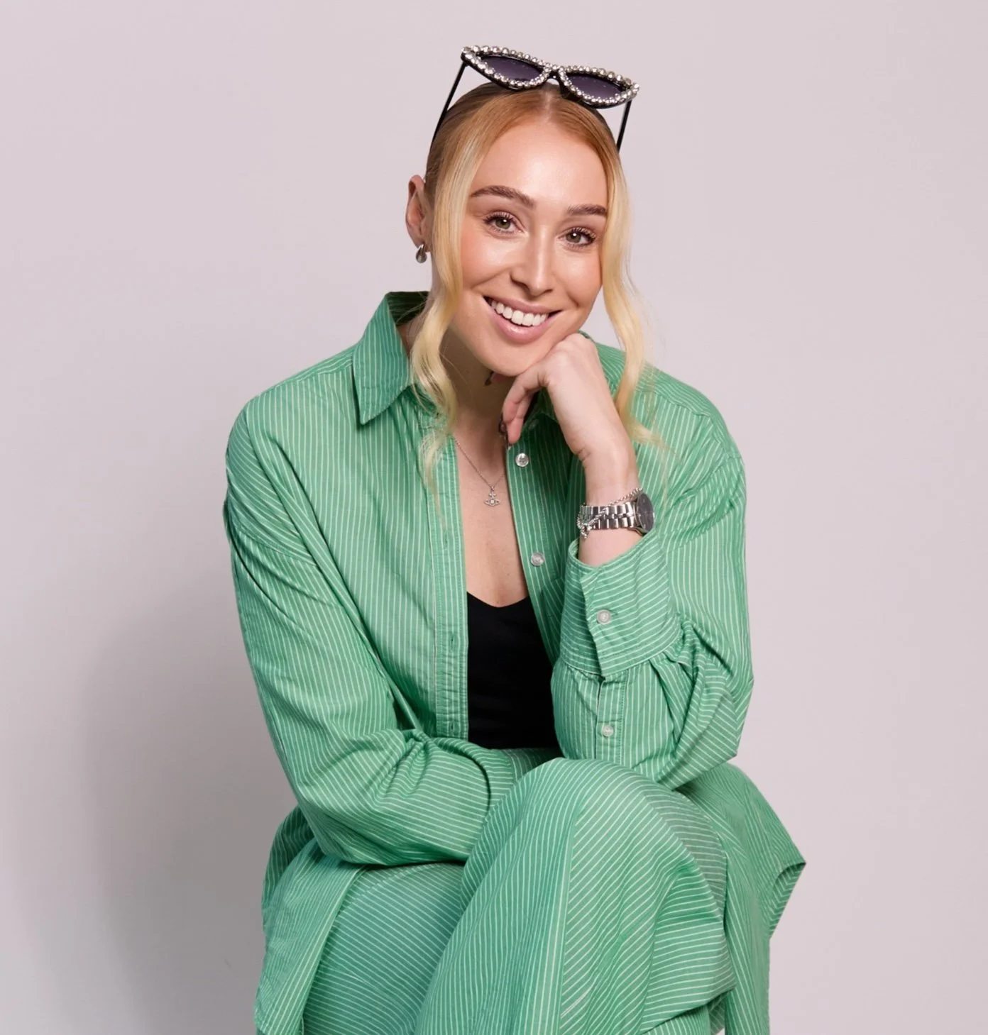 Celebrate with Hayley is wearing a green suit and smiling at the camera. She has some sunglasses on her head.