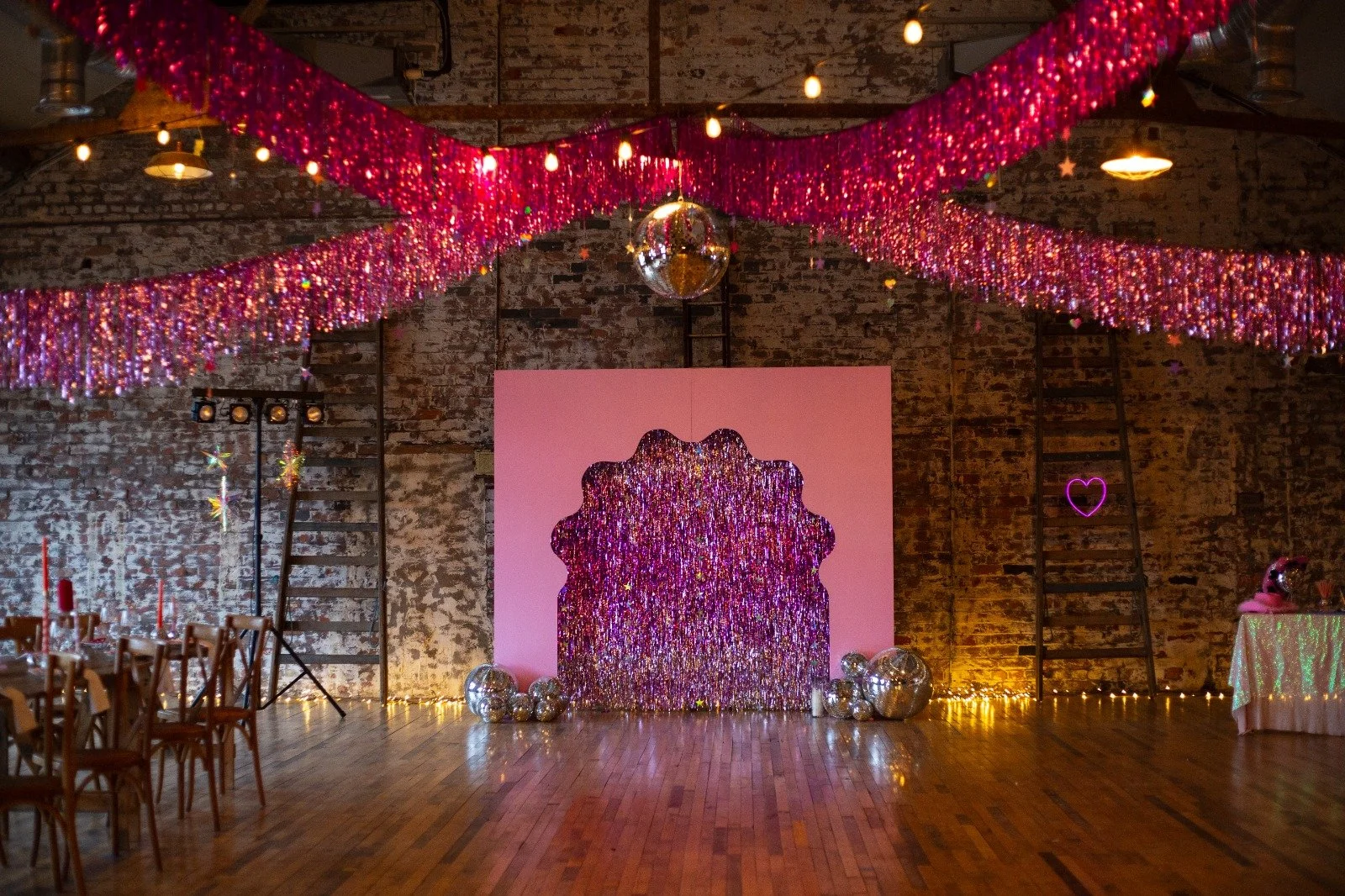 Pink tinsel ceiling swags and wavy backdrop with disco balls in an industrial wedding venue. Bold, retro wedding decor hire ideal for disco, party-style and alternative weddings.