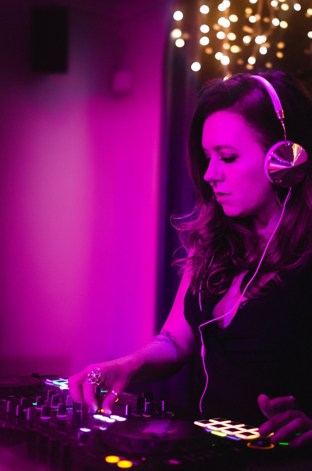 Rave The Date DJ Cara is immersed in the music, focused and glowing under rich pink and purple lights. The soft bokeh of fairy lights adds warmth to the scene as she works the decks with effortless confidence, perfectly capturing the vibrant and soul