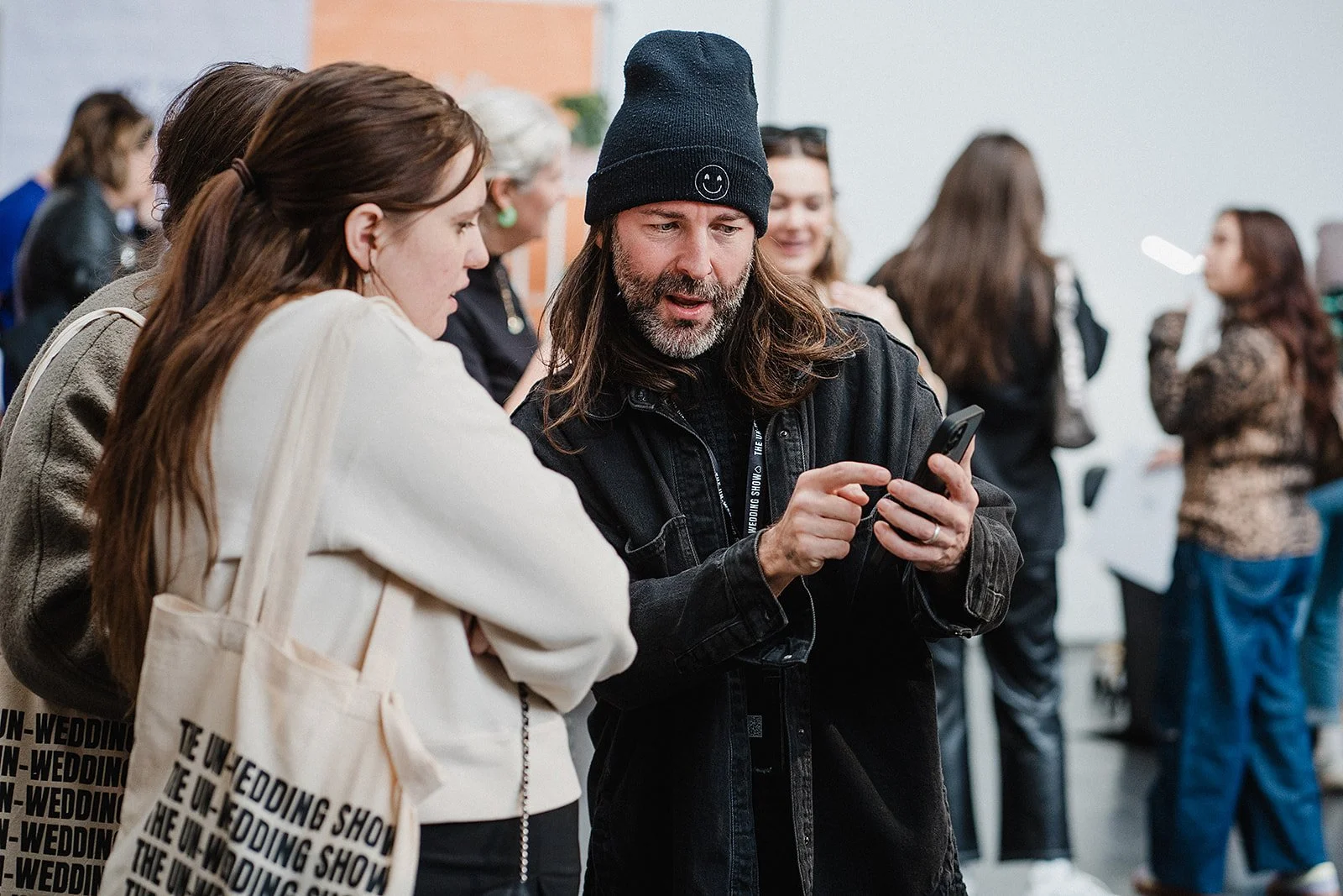 A wedding supplier with a black hat and beard is helping a bride to be at a wedding fair.