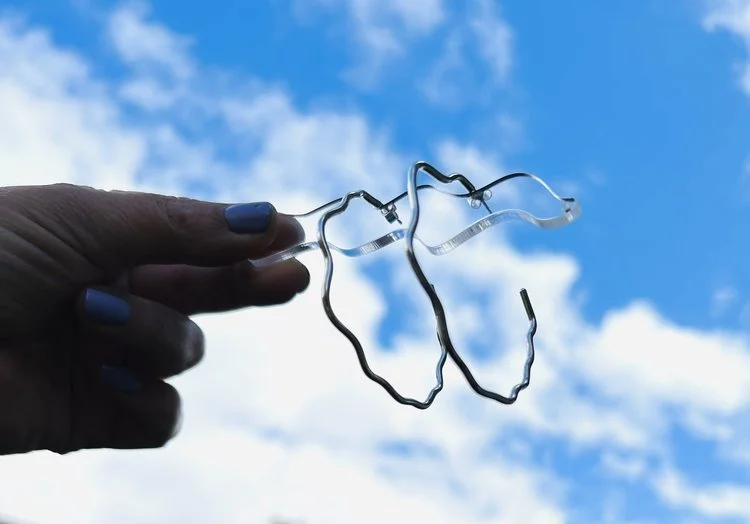 Statement wavy hoop earrings by Stacey Hill Jewellery held against a bright blue sky. Handcrafted in the UK, these cloud-inspired silver earrings capture a playful, modern bridal aesthetic.