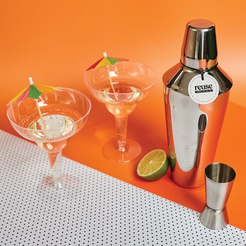 Two cocktail glasses with mini umbrellas beside a silver shaker, jigger, and lime half, styled by Melon Teaspoon for fun party and celebration accessories.
