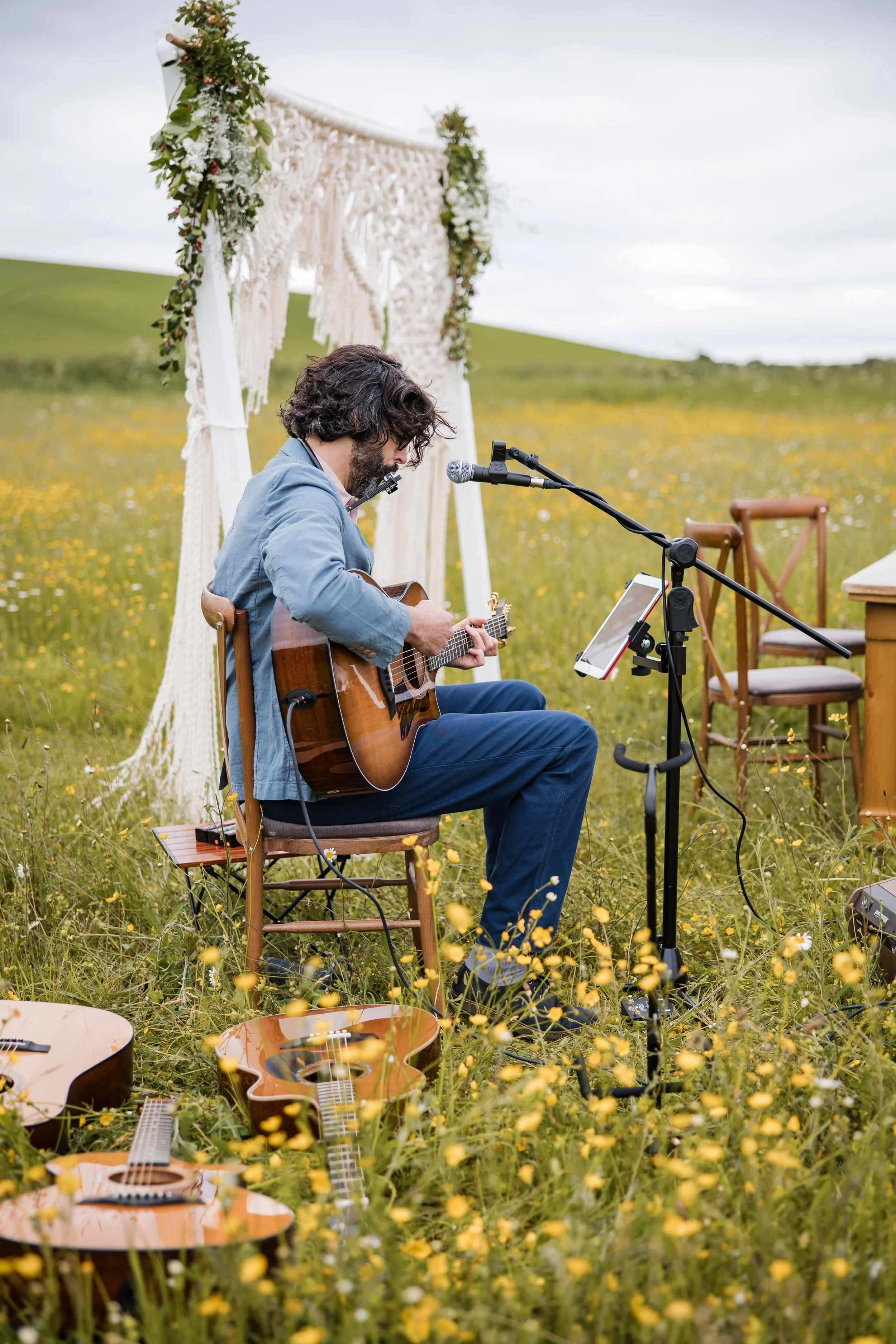 Thomas J Wilman, an acoustic wedding singer and guitarist, performs live at an outdoor ceremony surrounded by wildflowers and countryside views. His soulful acoustic music creates a relaxed, romantic atmosphere for couples and guests alike. Greg Shin