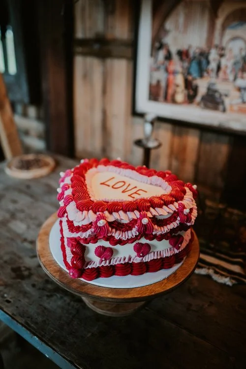 This bold and romantic creation by Amber’s Cakes and Treats embraces vintage charm with a playful twist. The heart-shaped cake, adorned with rich red and pink piped buttercream details, evokes a nostalgic, retro feel - perfectly suited for couples wh