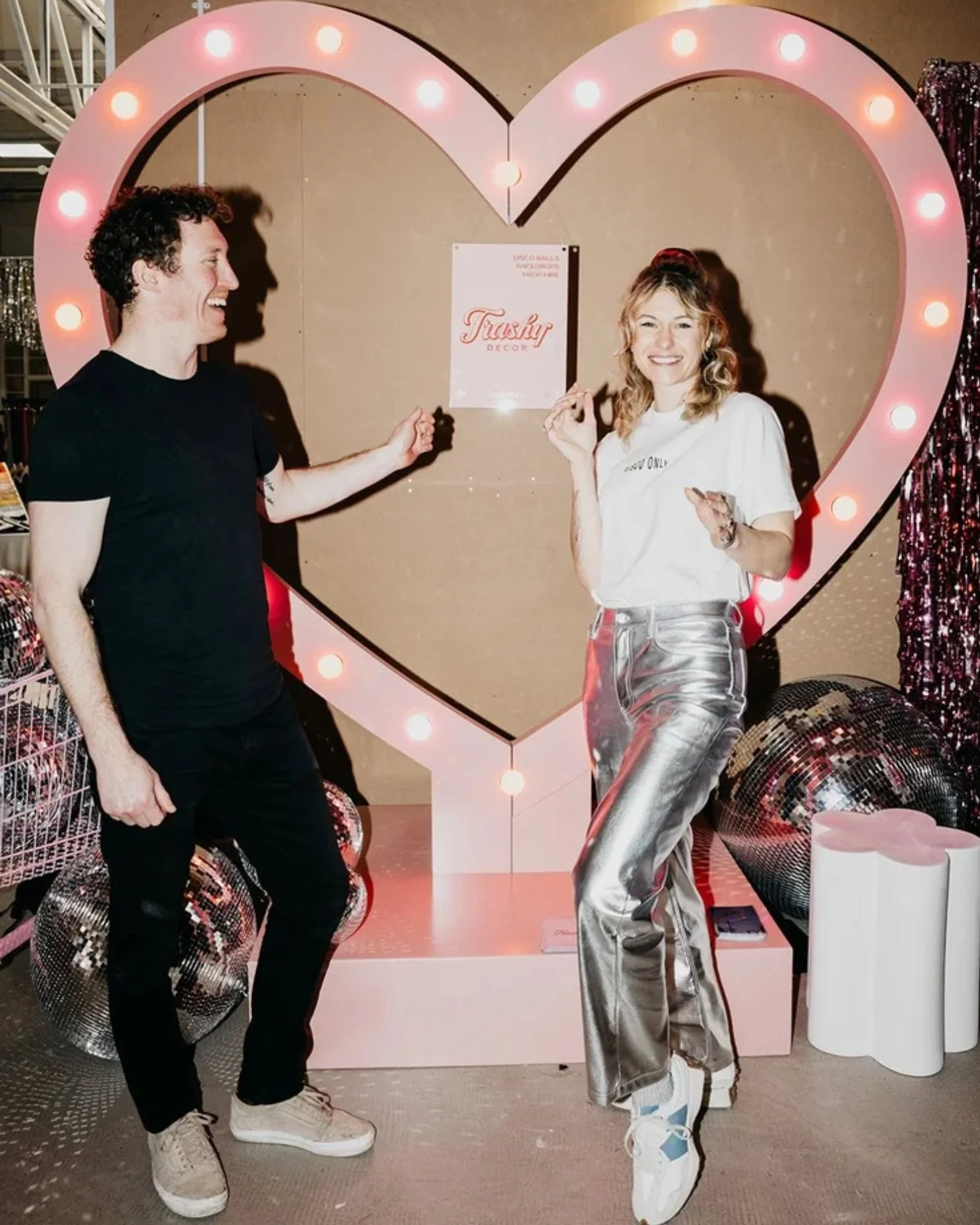 Aisling and Jack from Trashy Decor are standing in front of their Vegas Heart wedding ceremony backdrop.