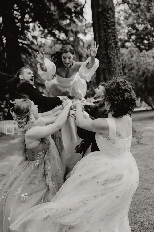 A joyful, high-energy moment captured by F.D Young Photography: the bride mid-air as her loved ones launch her upward in a burst of laughter and celebration. The black-and-white edit heightens the drama and emotion, highlighting the movement, the exp