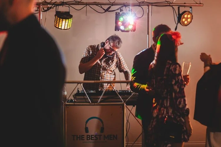 A DJ from The Best Men performs at a lively wedding reception, mixing crowd-favourite tracks and creating an energetic atmosphere for guests on the dance floor. With colourful disco lighting and a professional sound setup, The Best Men bring the ulti