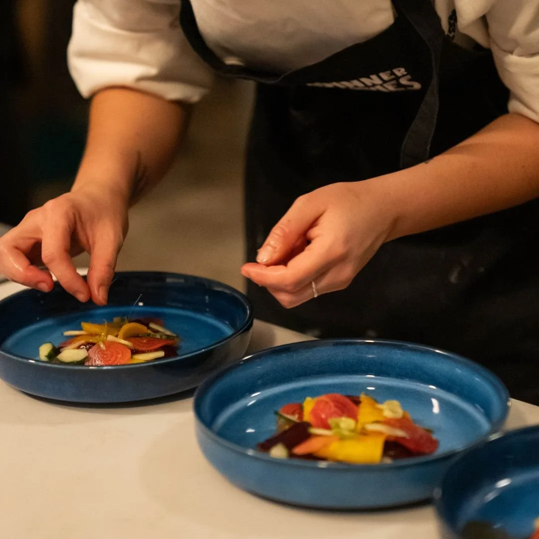 A Dinner Ladies chef is garnishing some blue bowls of colourful salad.