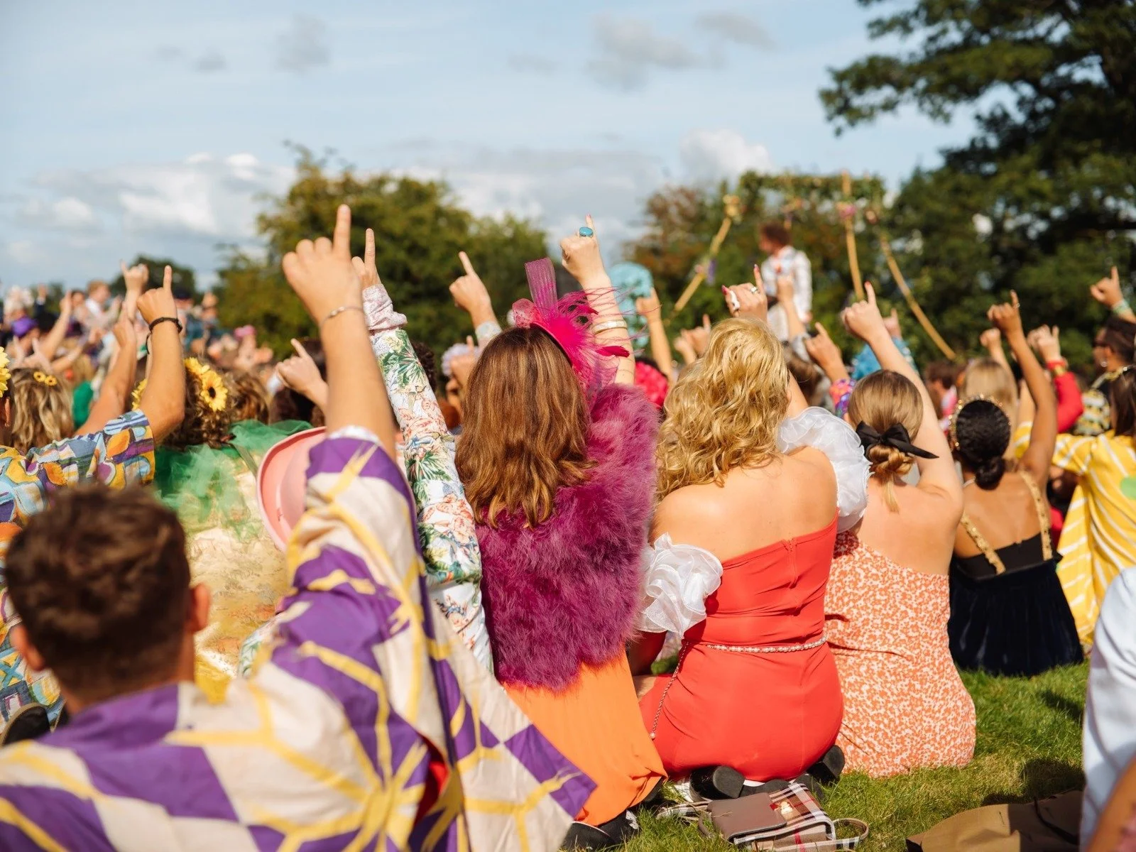 Outdoor festival-style wedding ceremony led by celebrant Lonan Jenkins, with guests seated on grass, cheering and raising their hands in celebration. A colourful moment full of energy, connection and relaxed vibes, capturing a non-traditional wedding