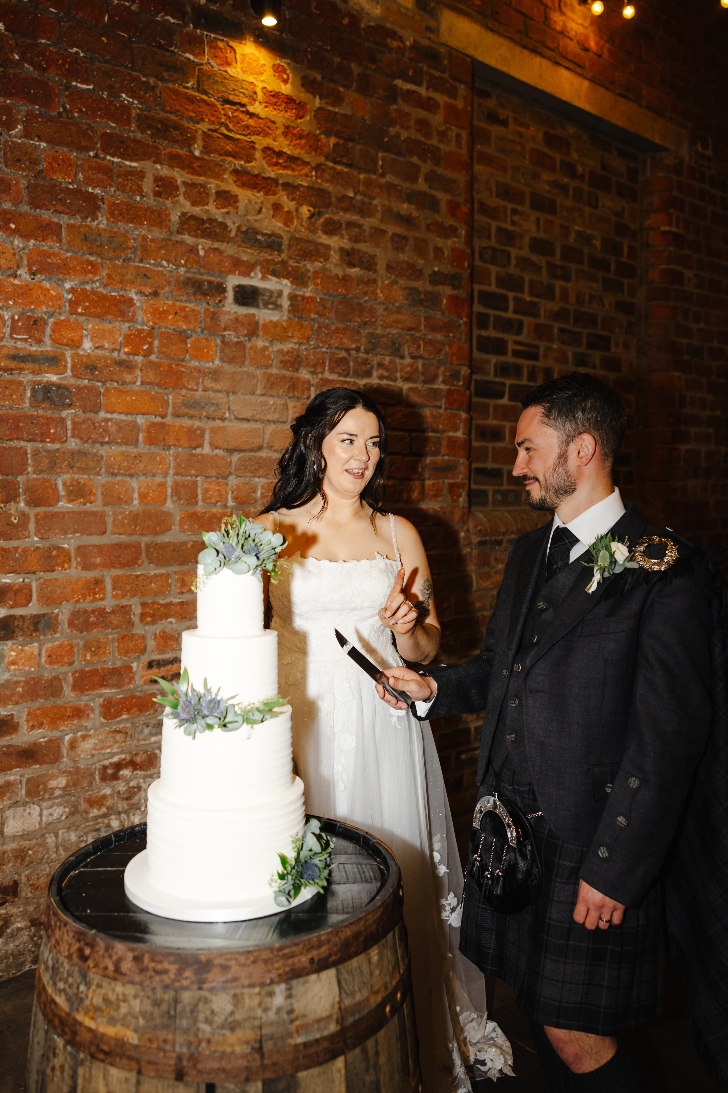 Marie looks at Oliver, who is holding a knife, preparing to cut the large white wedding cake, made by Liggy's Cakes.