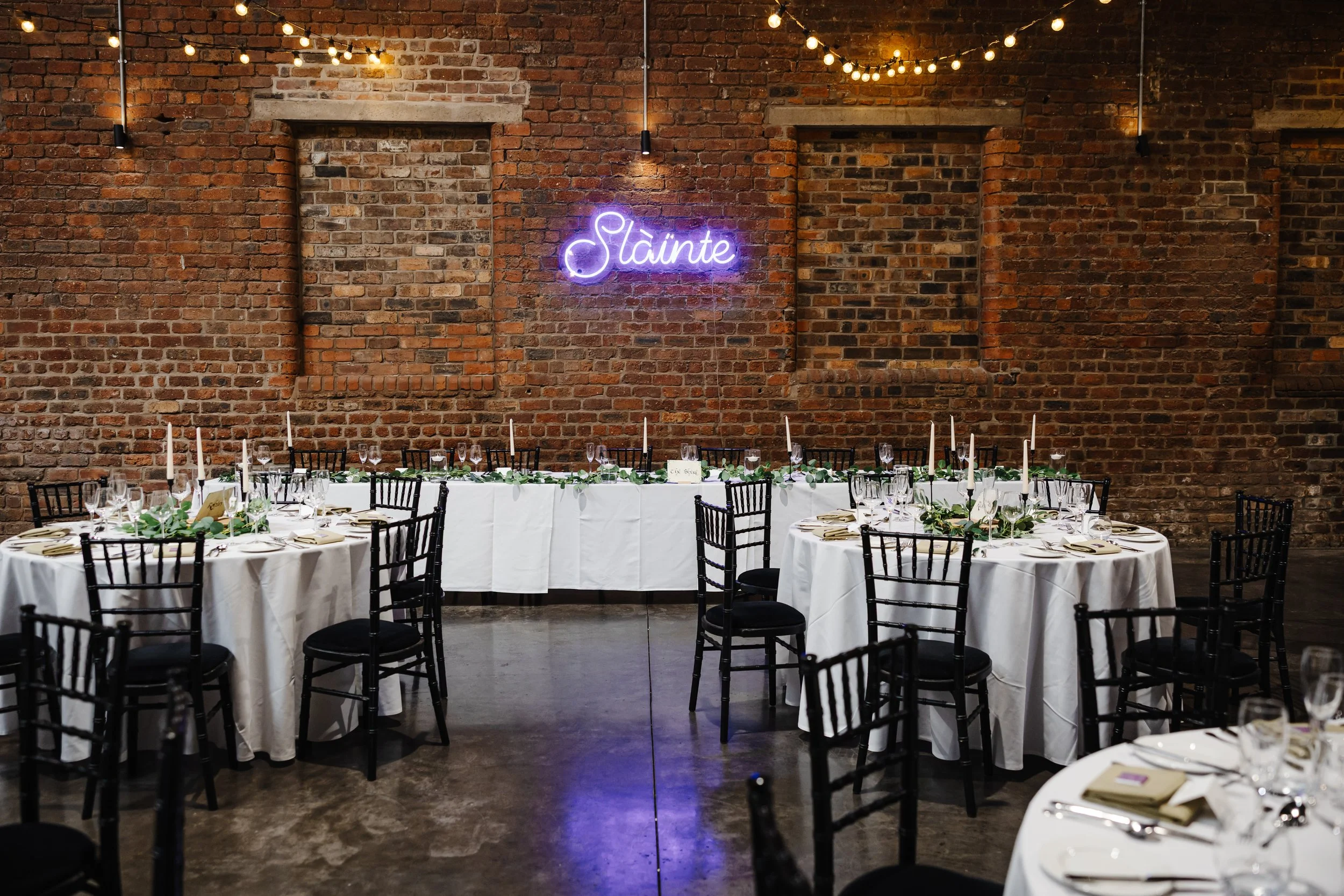 Tables set and ready for the Wedding dinner. A neon sign on the wall reads 'Slainte' - gaelic for 'Cheers!'