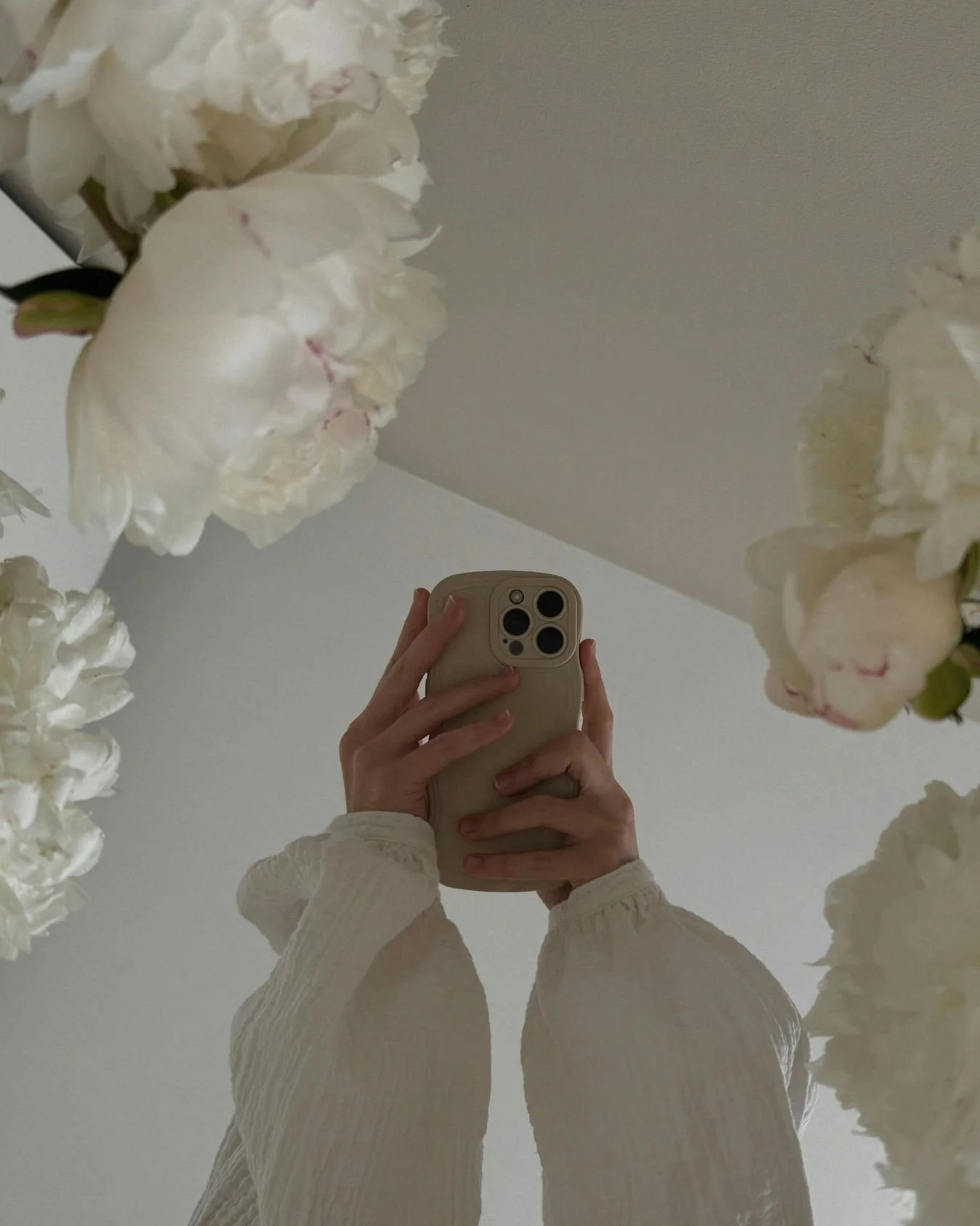 A wedding content creator's hand is holding up a white mobile phone and taking pictures of some flowers..