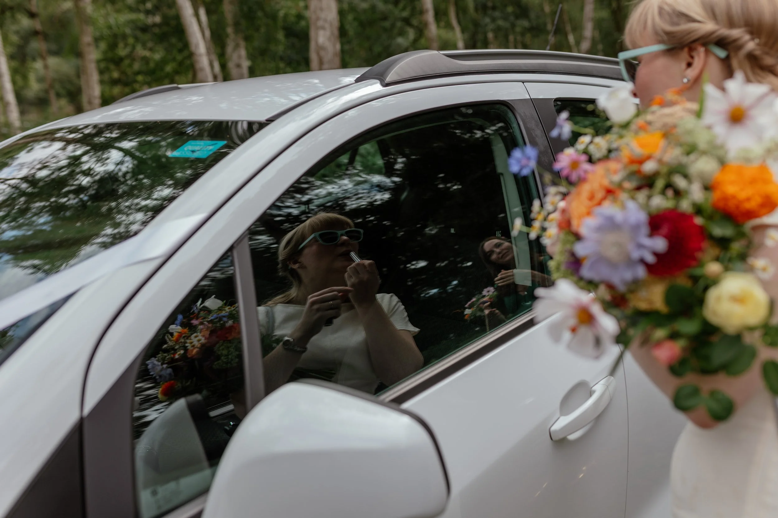 A white wedding car with the bride doing her lipstick in the window.