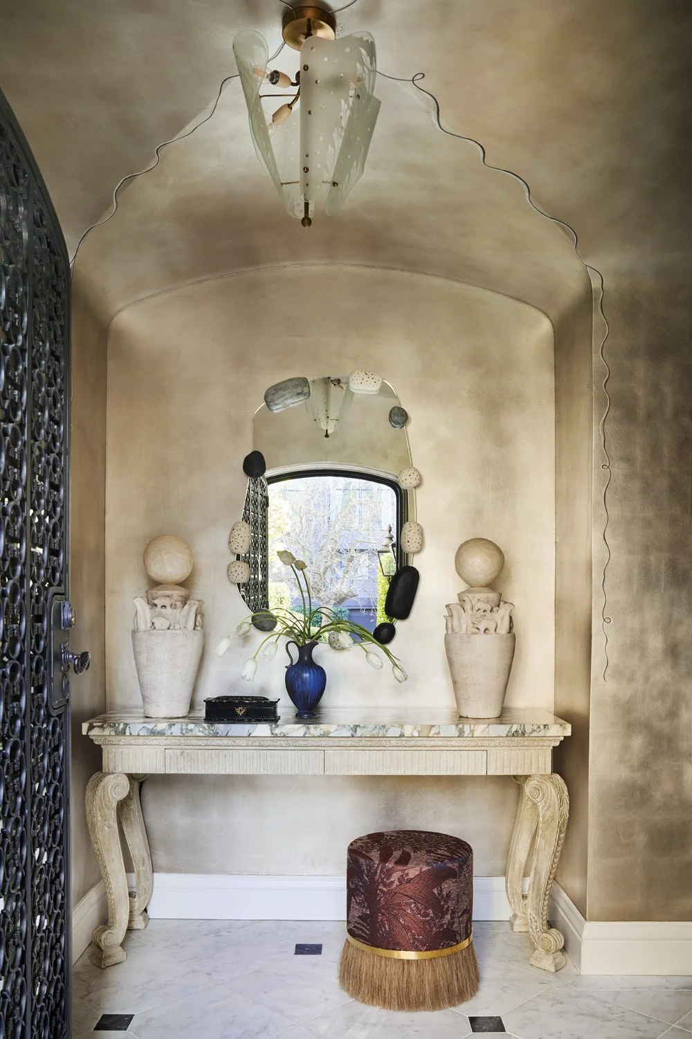 Entryway into a San Francisco home in Presidio Heights that has a shimmering aluminum leaf ceiling with hand-painted details and a console table styled with vases and flowers.