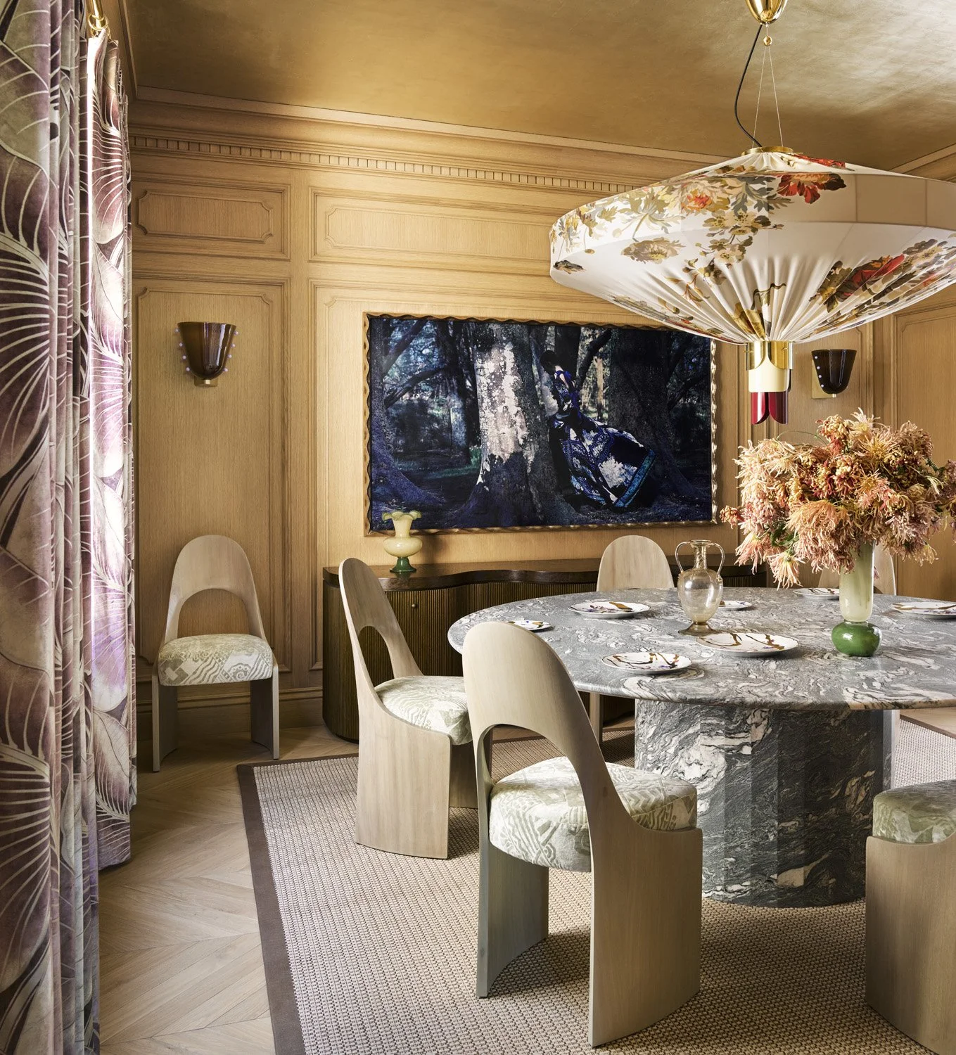 Wood paneled dining room with gold ceiling, large stone dining table, and floral pendant light.