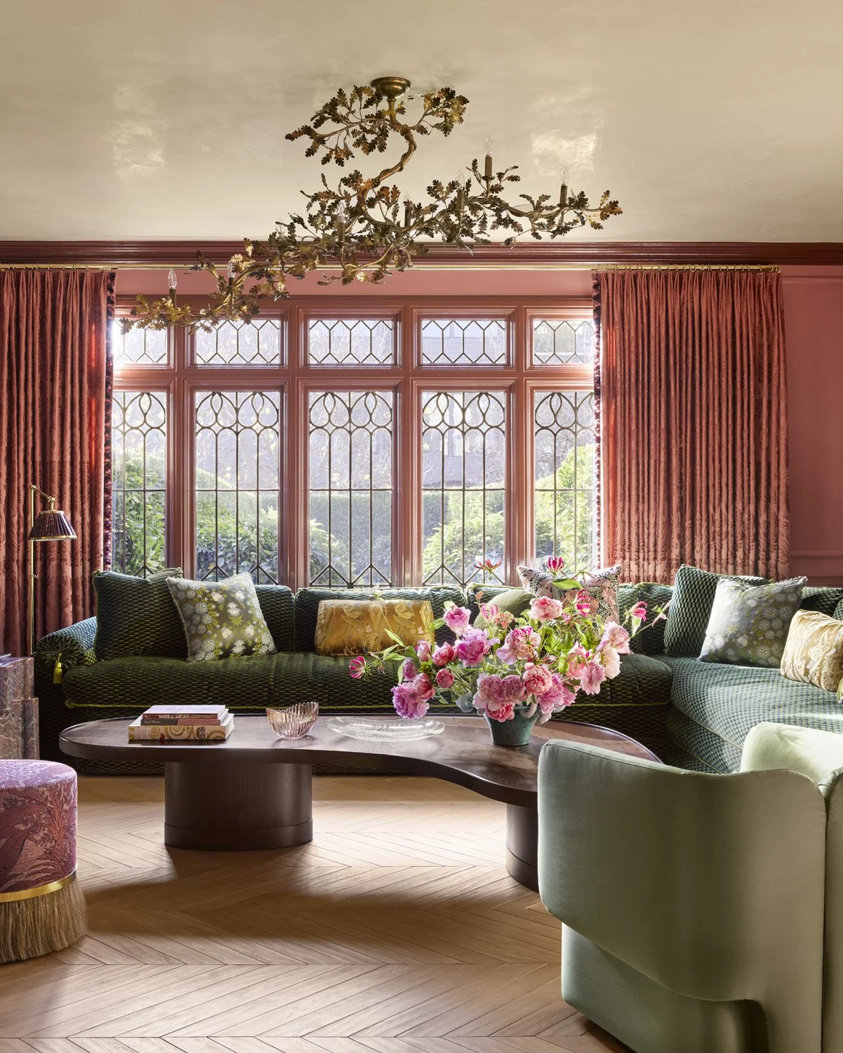 Pink and green parlor living room in San Francisco home with original leaded windows, a pale parquet wood floor and an ottoman style green custom couch.