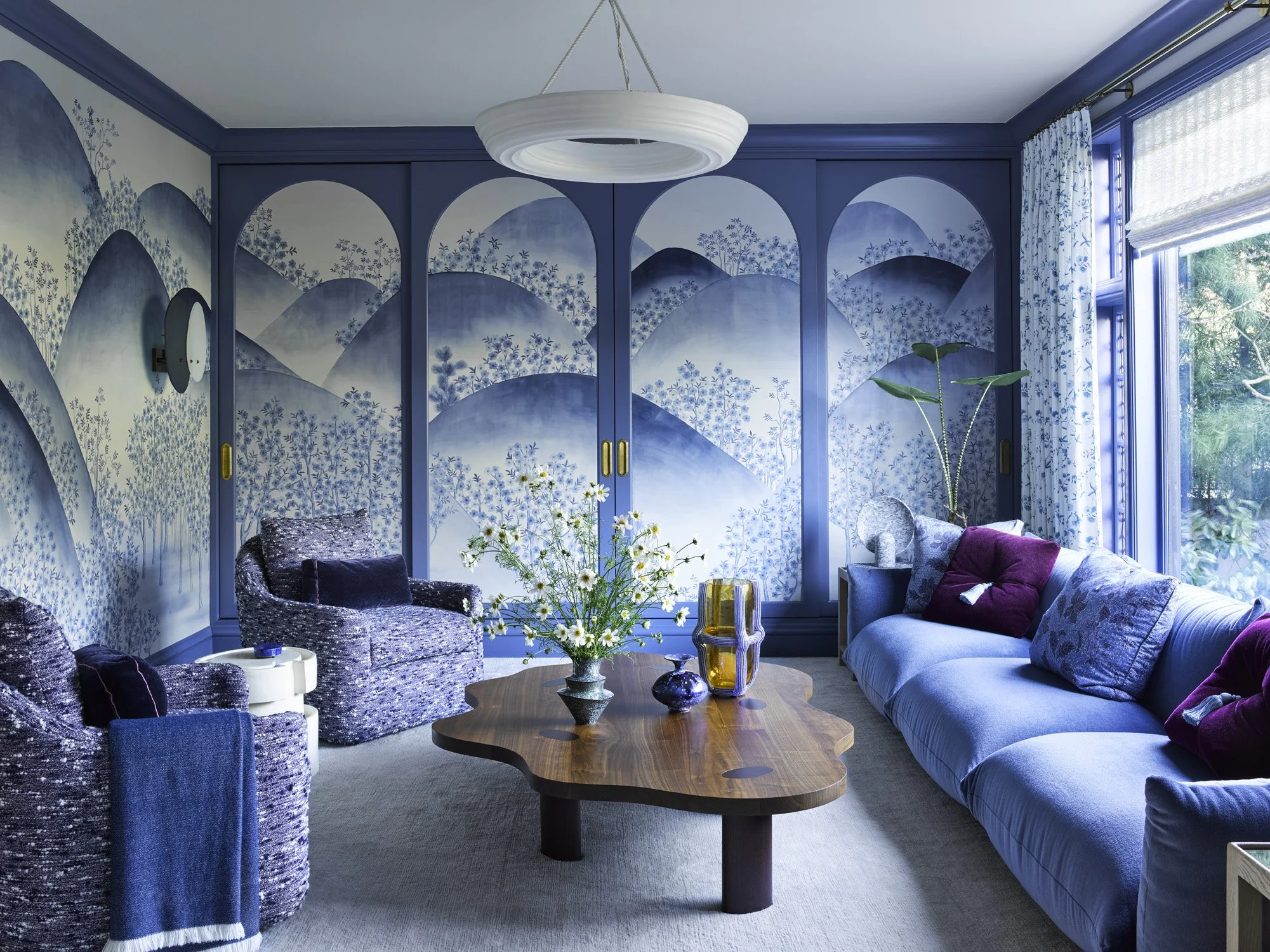 Indigo family room with Shoji screen mechanism to hide tv and de Gournay wallpaper, with organic shapes like a wavy coffee table and comfortable seating.