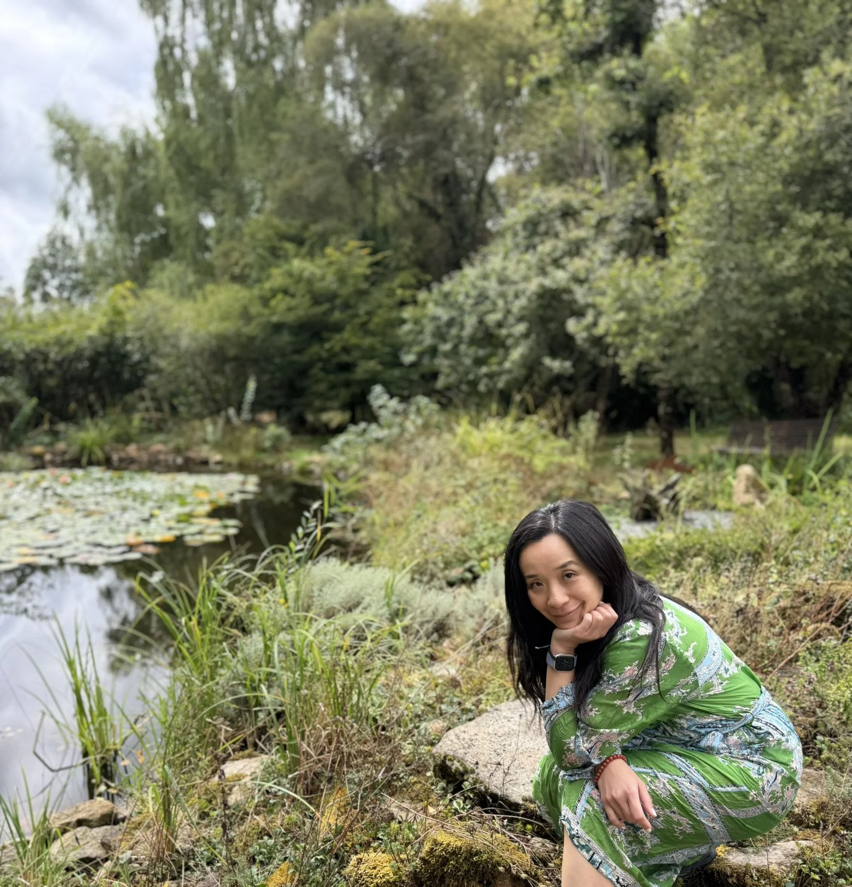 Li Lamb, hypnotherapist based in Ilkley, Yorkshire, kneeling by a peaceful pond surrounded by nature, reflecting her calming, holistic approach to emotional healing and subconscious re programming therapy