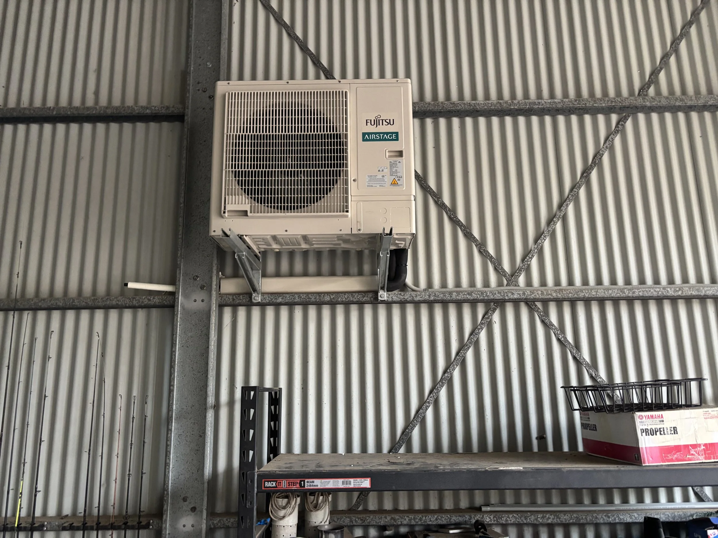 Industrial air conditioning unit mounted on a metal wall in a garage or workshop.