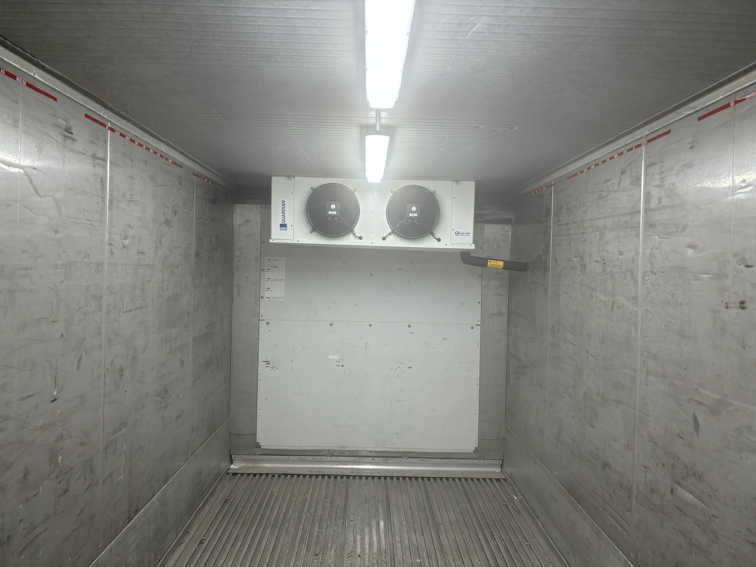Inside view of an empty refrigerated truck with metal walls, ceiling, and floor, containing an air conditioning unit at the front.