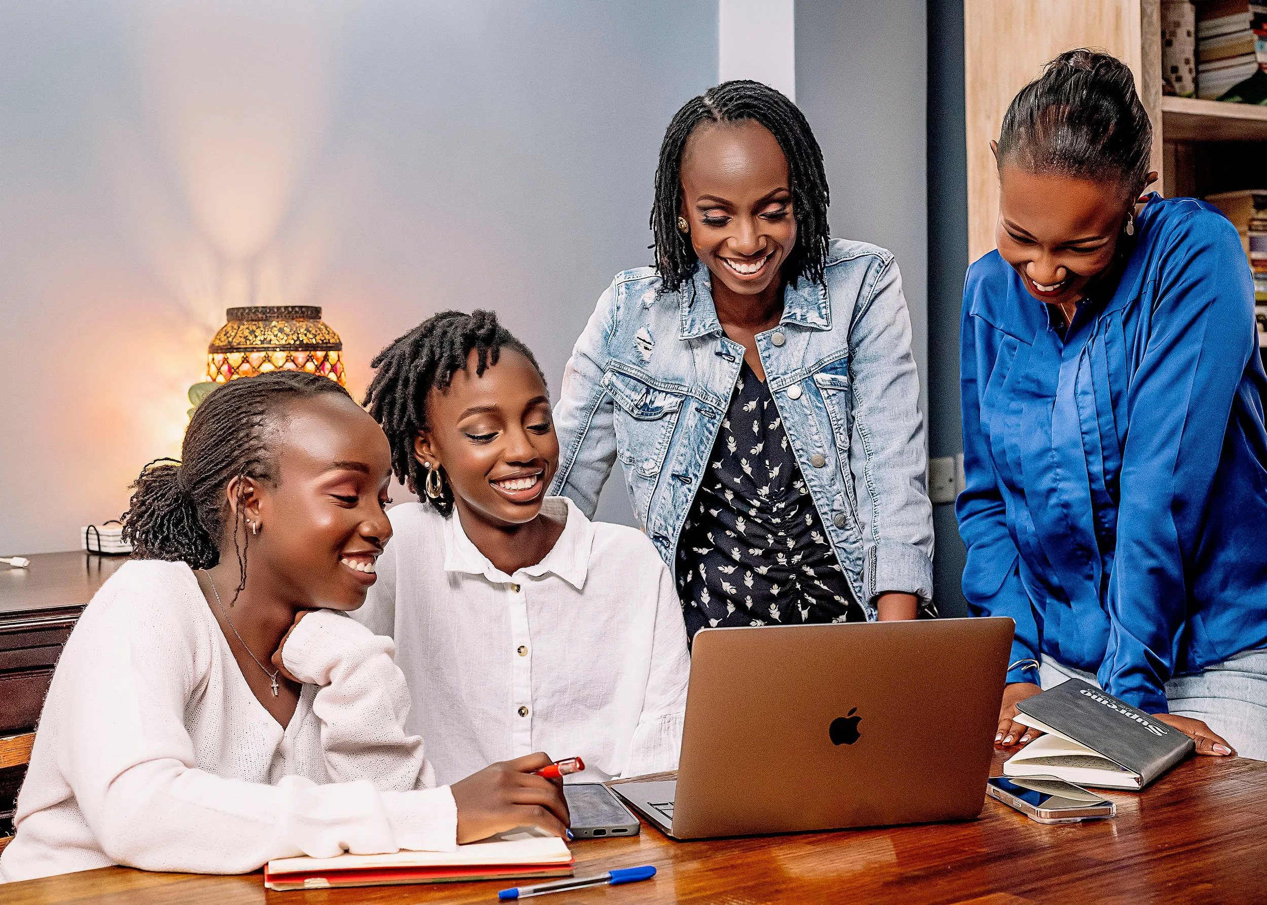A team of women working together around a laptop during a business planning session, illustrating collaborative virtual support and operations management.