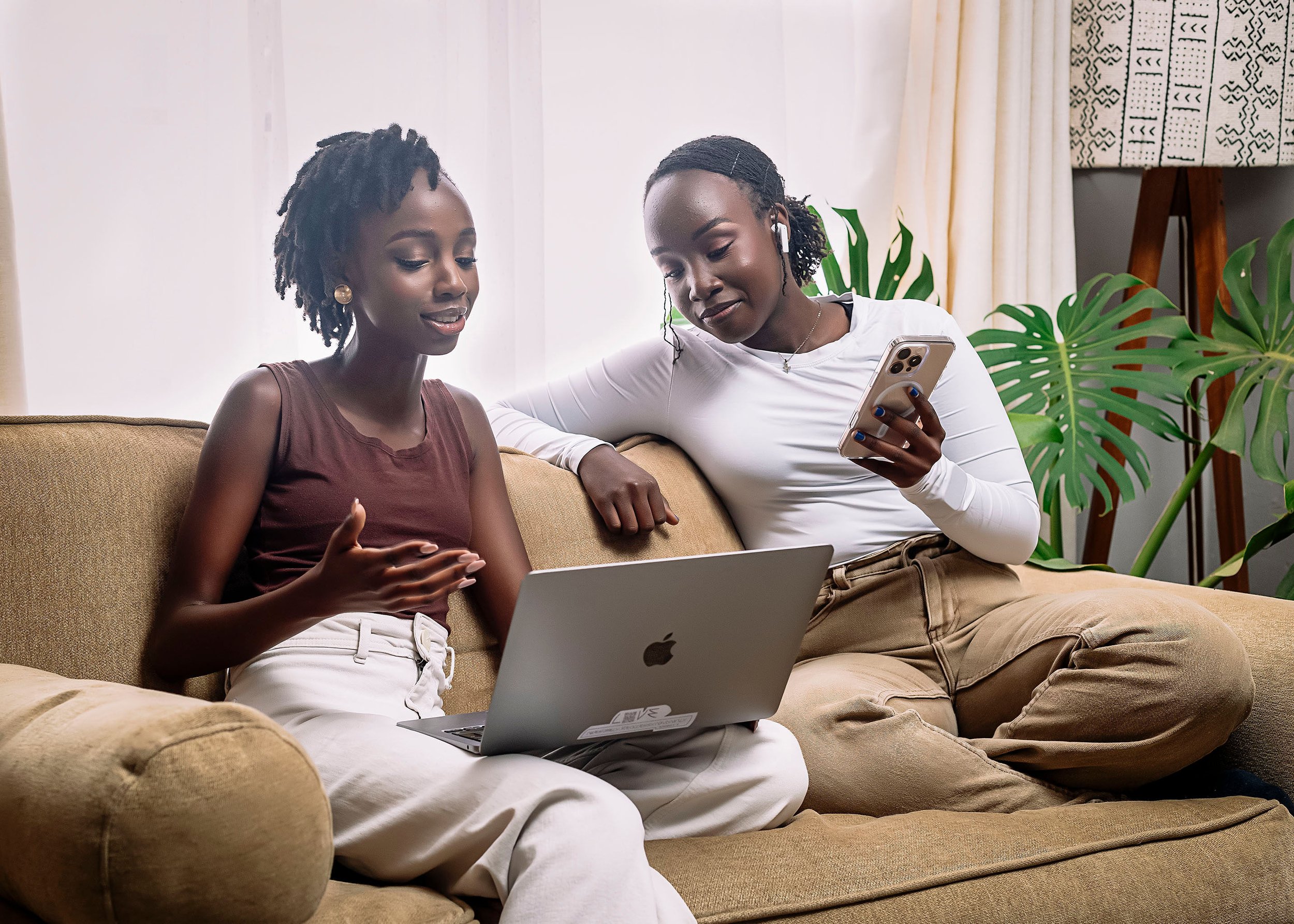 Two women collaborating remotely while reviewing business tasks on a laptop and smartphone, representing virtual assistant support for entrepreneurs.