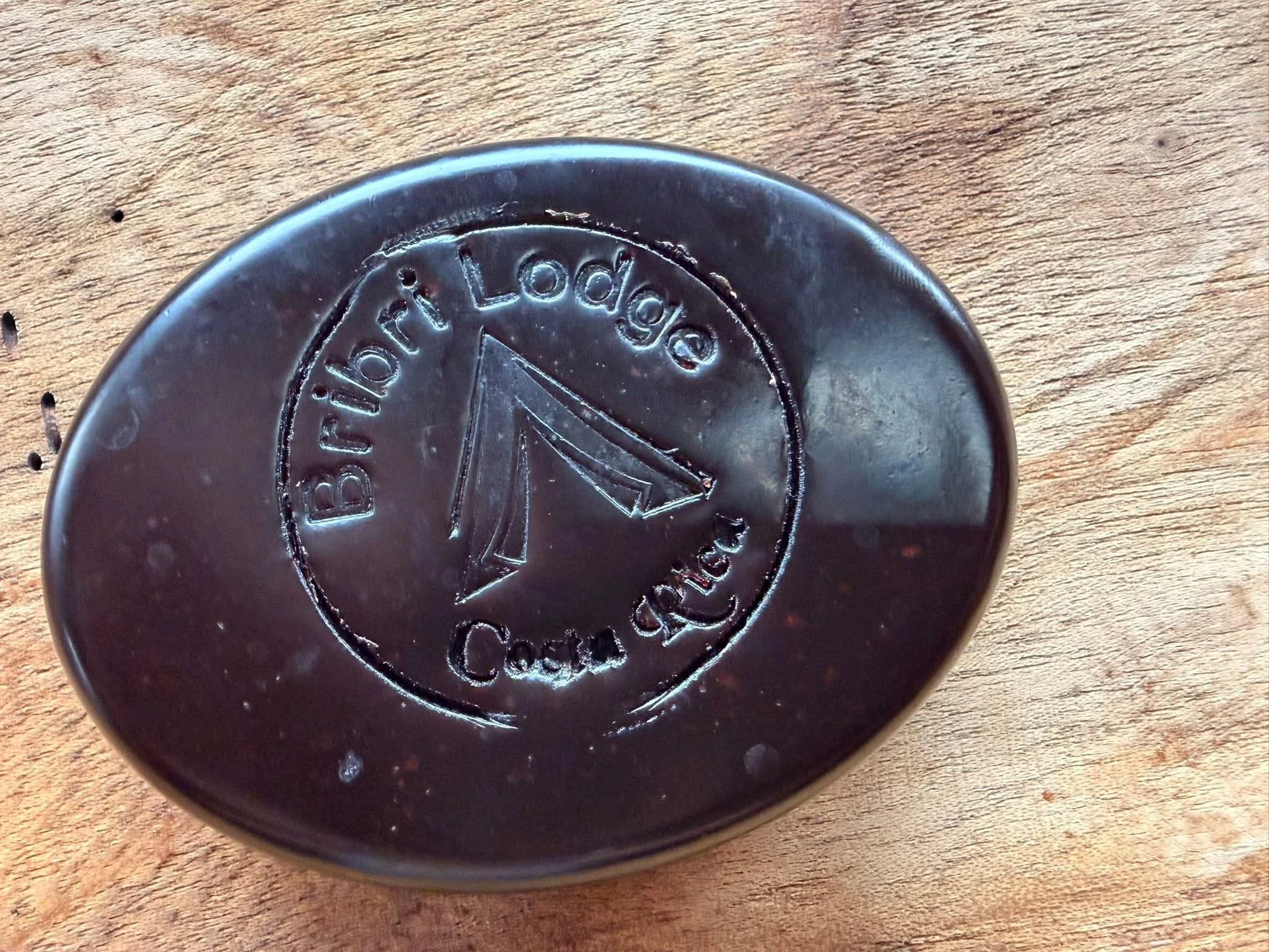 Close-up of a black, round object with carvings, including the word 'Babot' and an image of a sailboat on water, resting on a wooden surface.