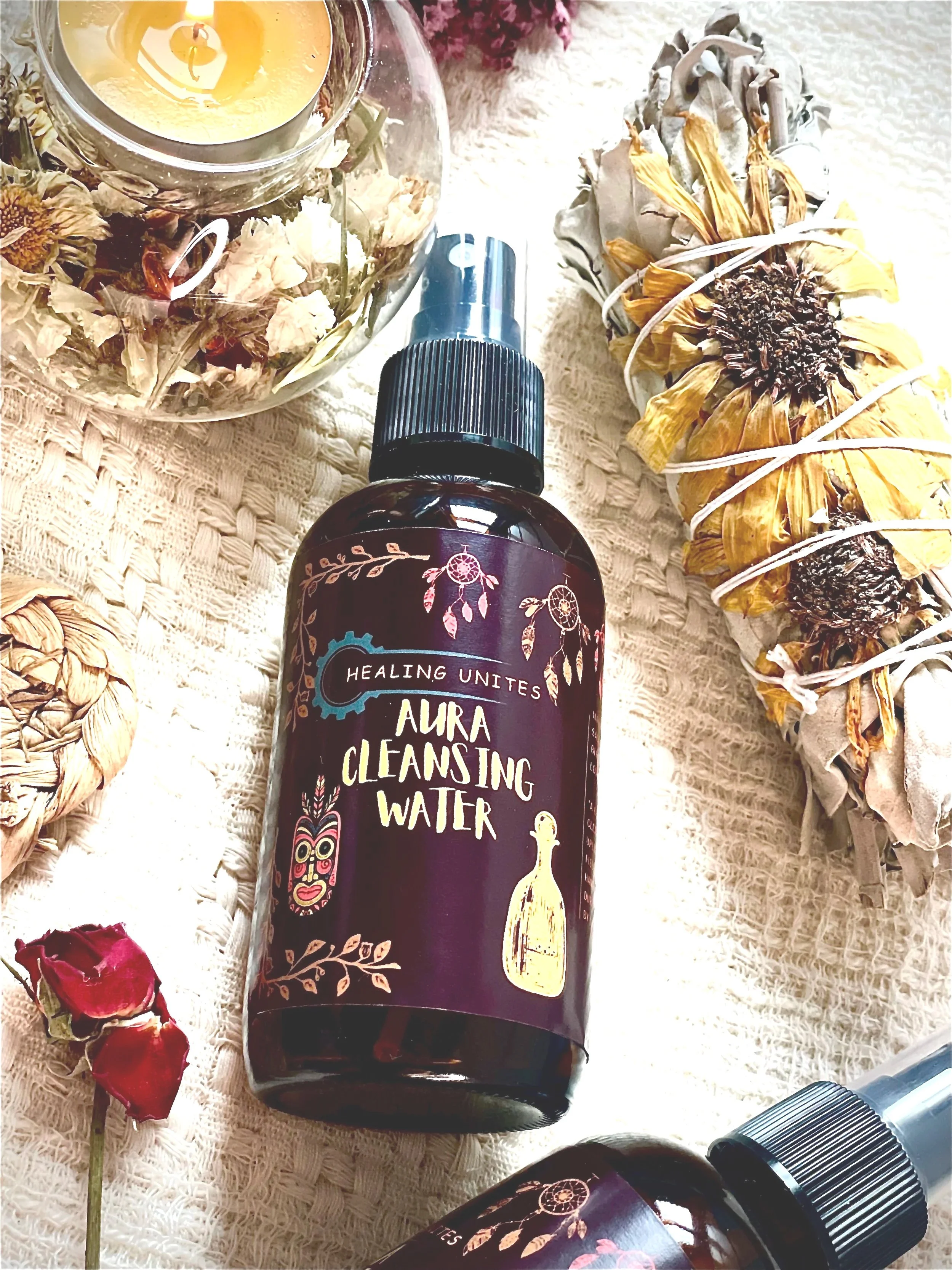 A bottle of aura cleansing water surrounded by dried flowers on a textured fabric surface.