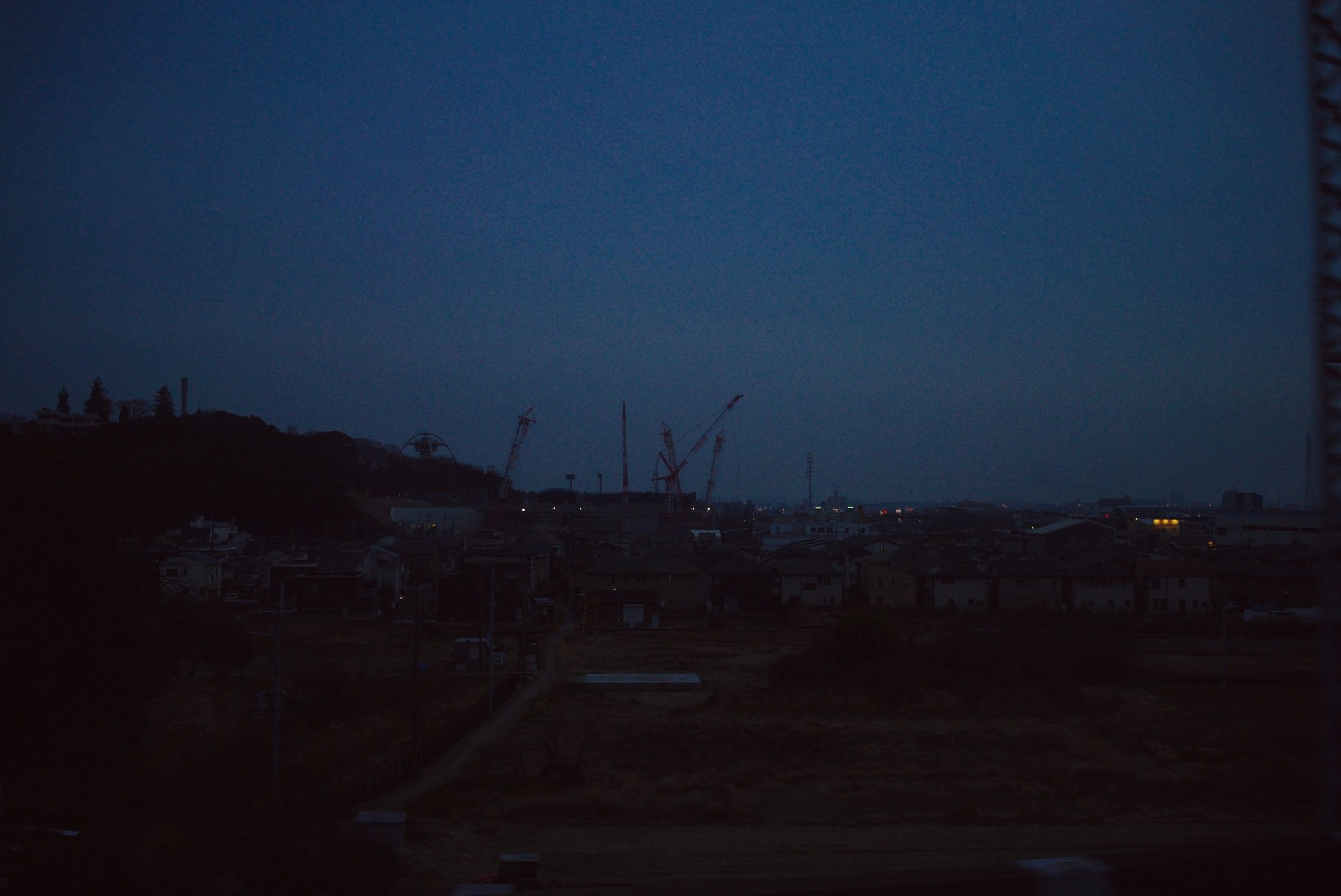 Nighttime cityscape with construction cranes and residential buildings under a dark sky.