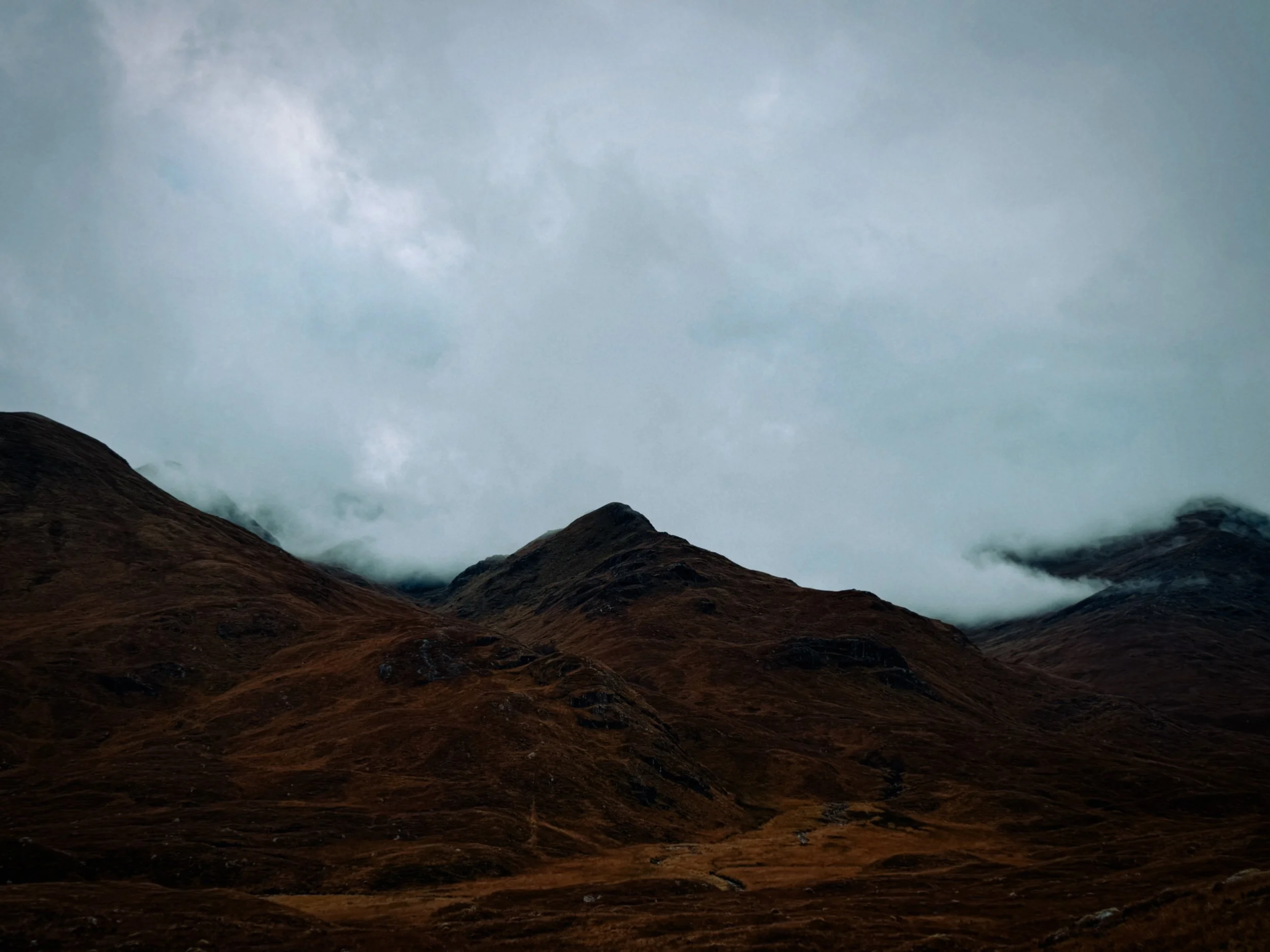 Brown mountain landscape with dark, weathered slopes and a cloudy sky overhead