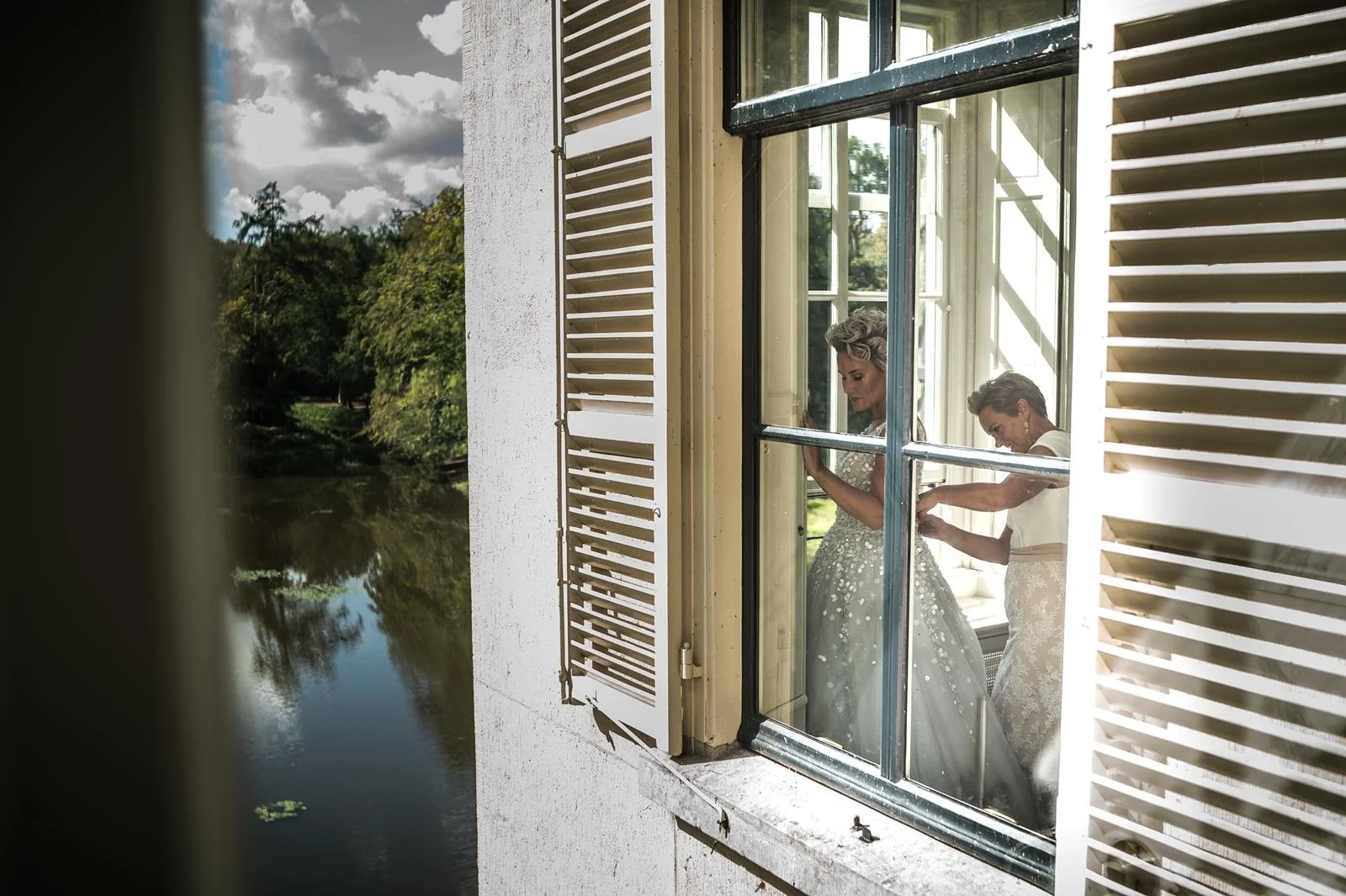 Mother helping her daughter with her wedding dress at Parc Broekhuizen, beautifully captured through a window.