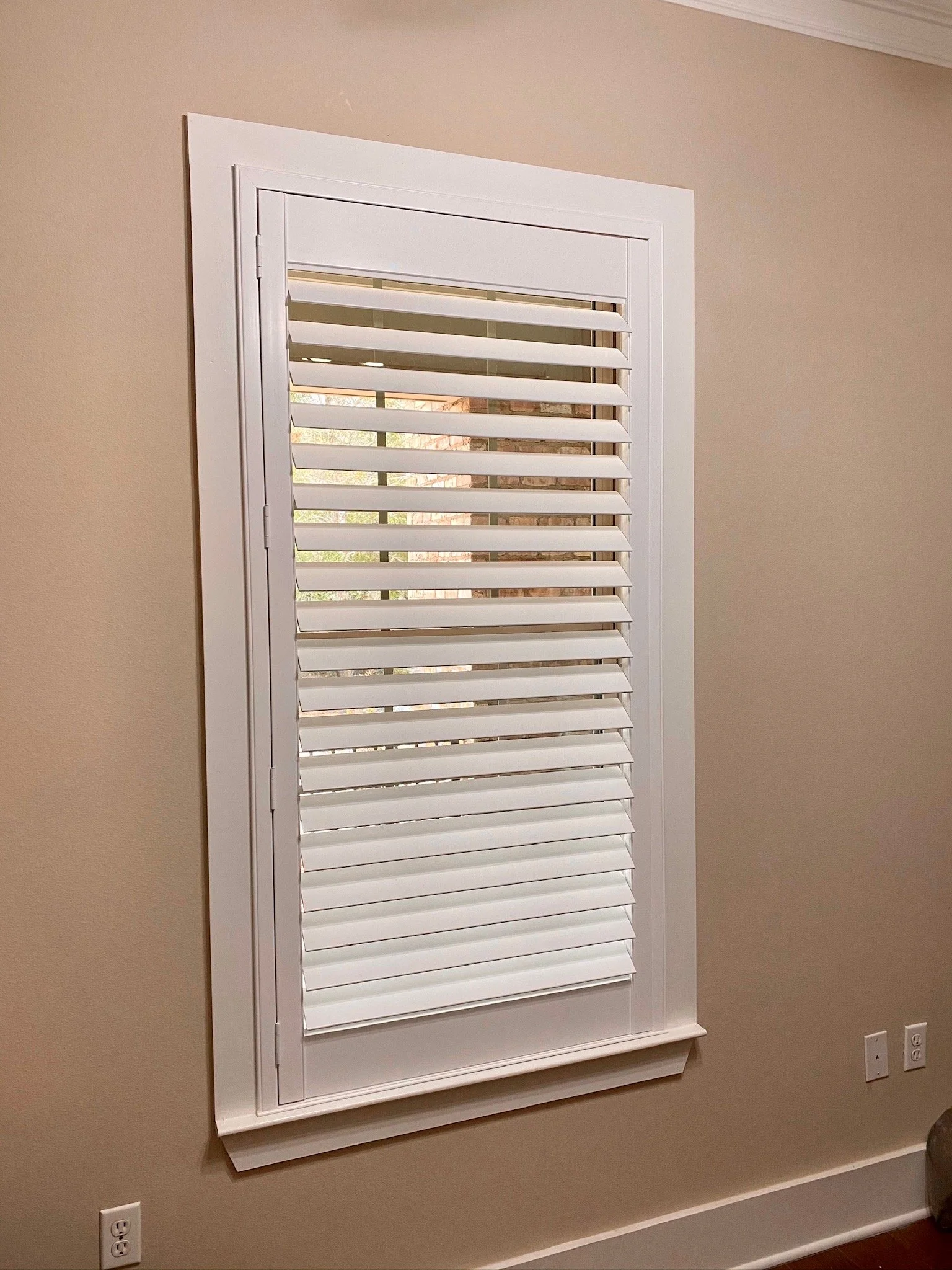 A window with white plantation shutters in a beige wall.