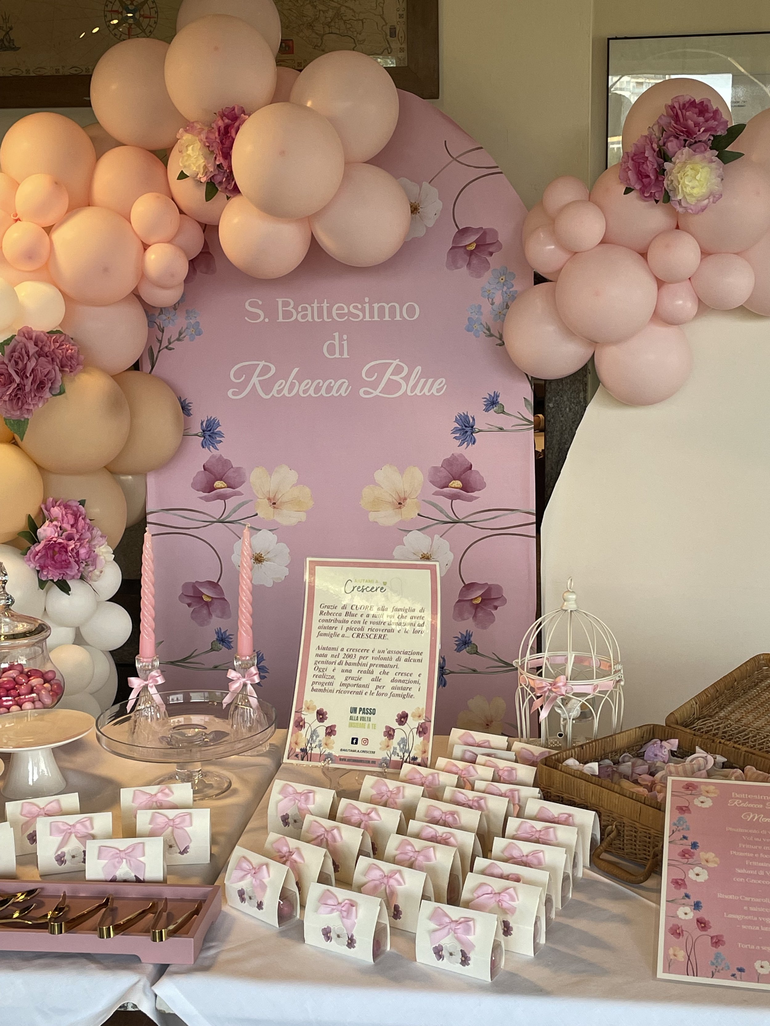 Decorazioni pastello rosa e bianco con palloncini e fiori per un battesimo, con tavolo di dolci e biglietti.