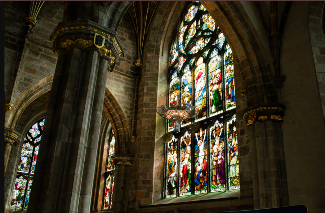 Intricate stained glass window and gothic stone pillars inside a historic Scottish cathedral.