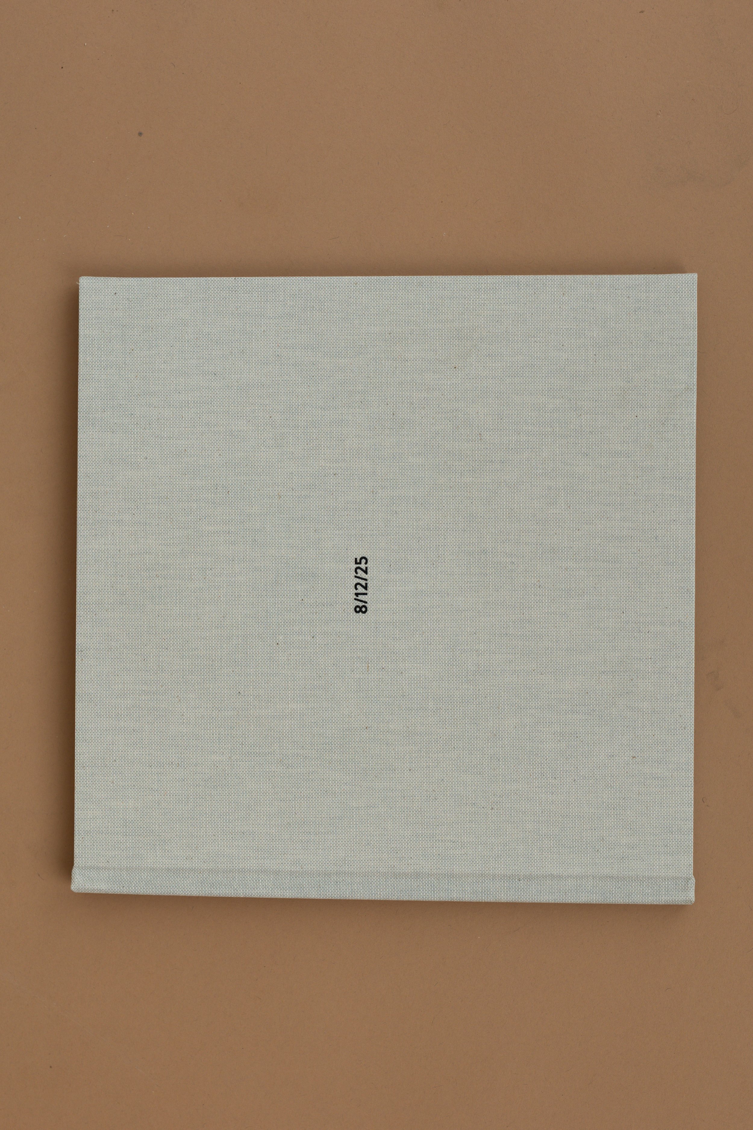 A white square paper with the date 8/12/25 printed in black, placed on a light brown surface.