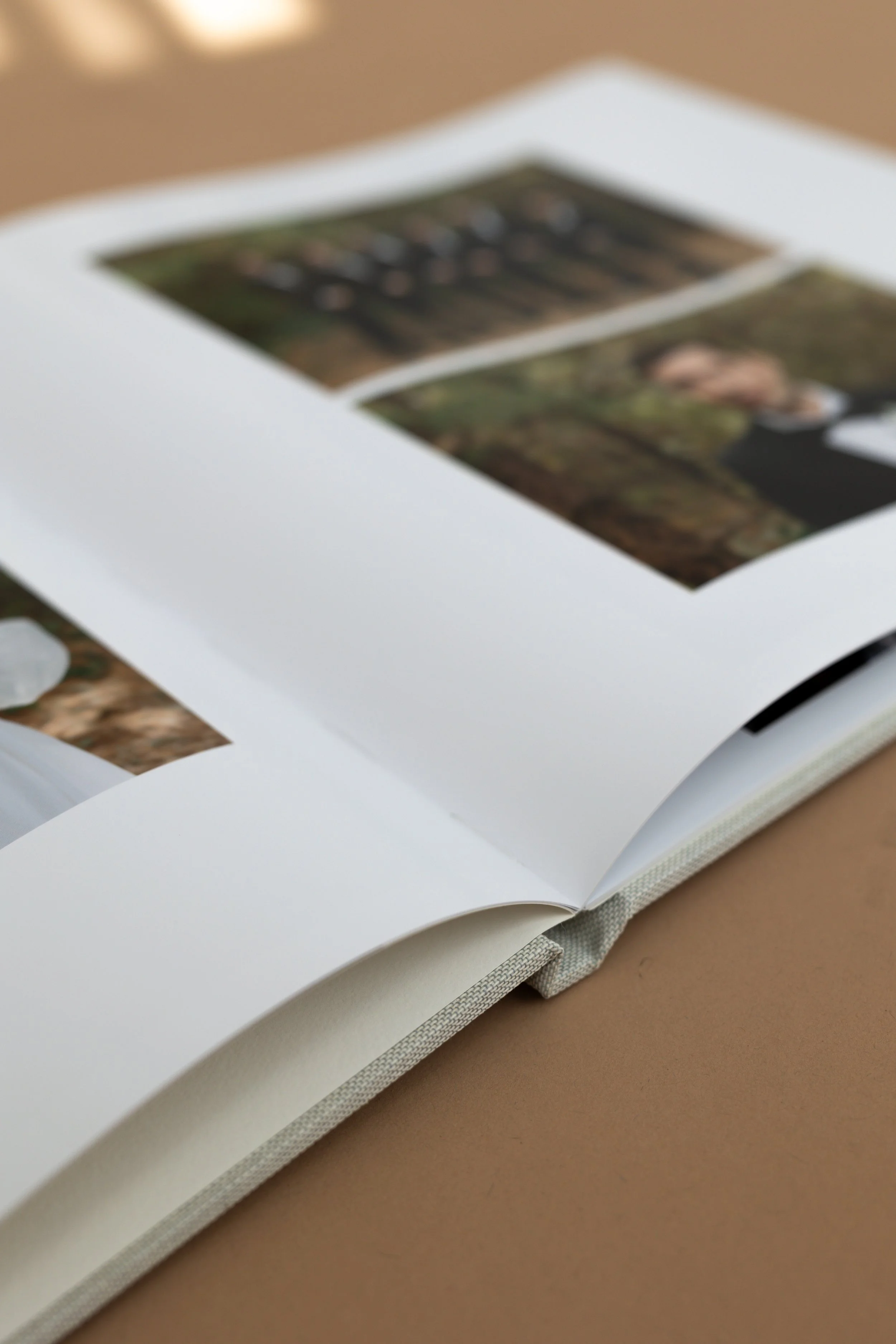 Close-up of an open photo album with white pages and pictures, placed on a brown surface.