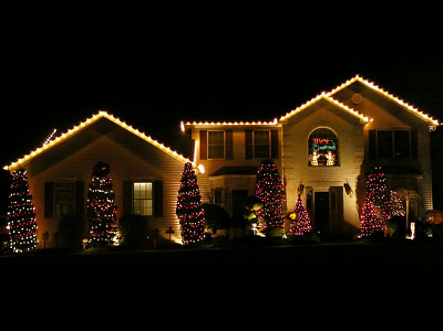 A two-story house decorated for Christmas with illuminated Christmas trees and string lights outlining the roof at night.