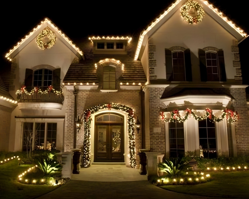A large, elegant house decorated with Christmas lights and wreaths at night.