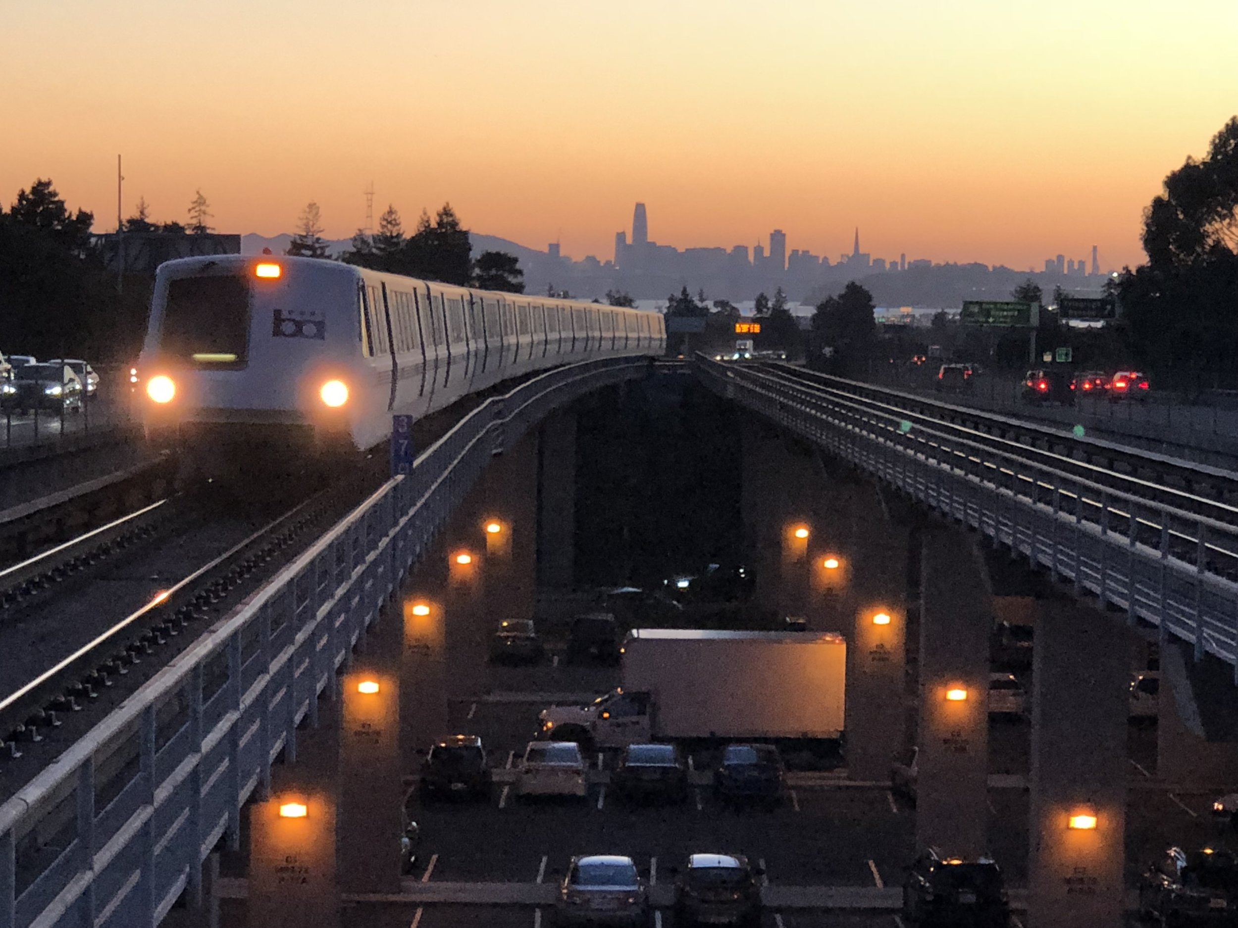 A train traveling on an elevated track with city skyline in the background at sunset.