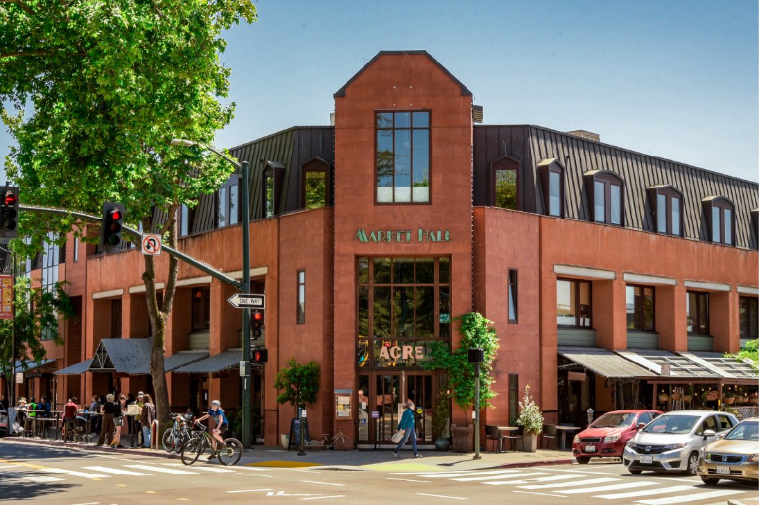 Street view of Market Hall building with pedestrians, bicycles, and parked cars in front.