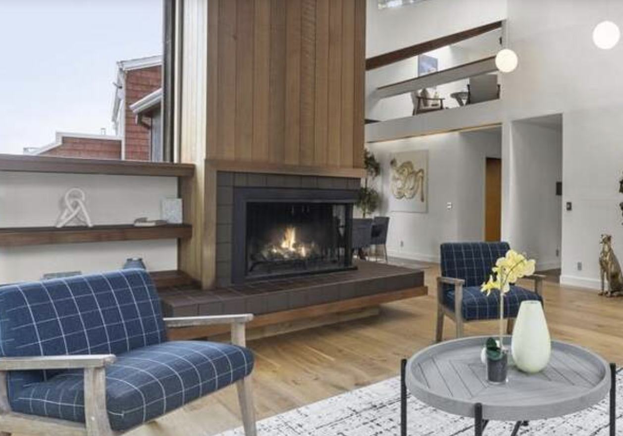 Living room with a modern fireplace, wooden and white walls, two plaid blue armchairs, a small round gray coffee table with a white vase and flowers, and a plush beige dog statue in the corner.