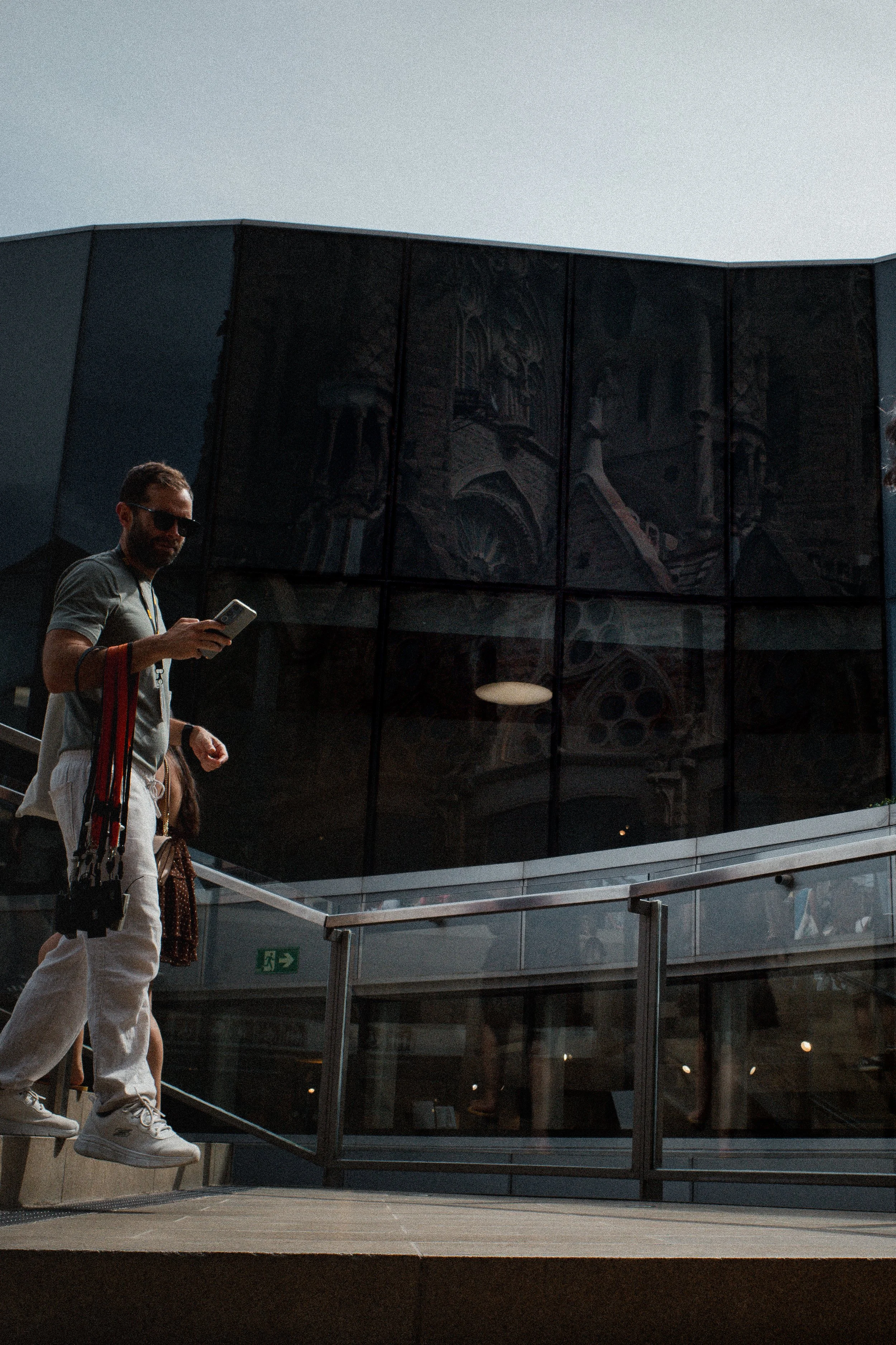 Un hombre baja unas escaleras de cristal y metal, con la fachada de la Sagrada Familia reflejada en los ventanales.