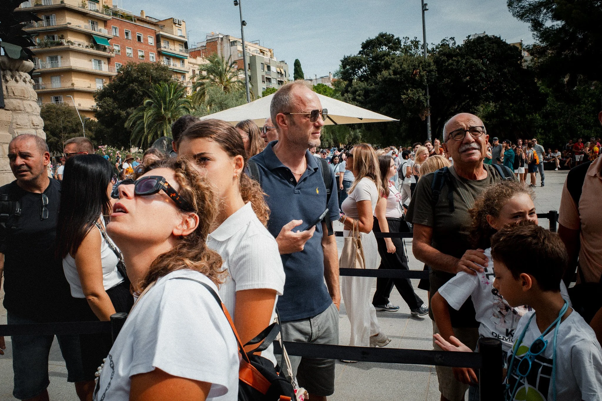Un grupo de turistas mira hacia arriba, hacia la fachada de la Sagrada Familia, con una mujer con gafas de sol en primer plano.