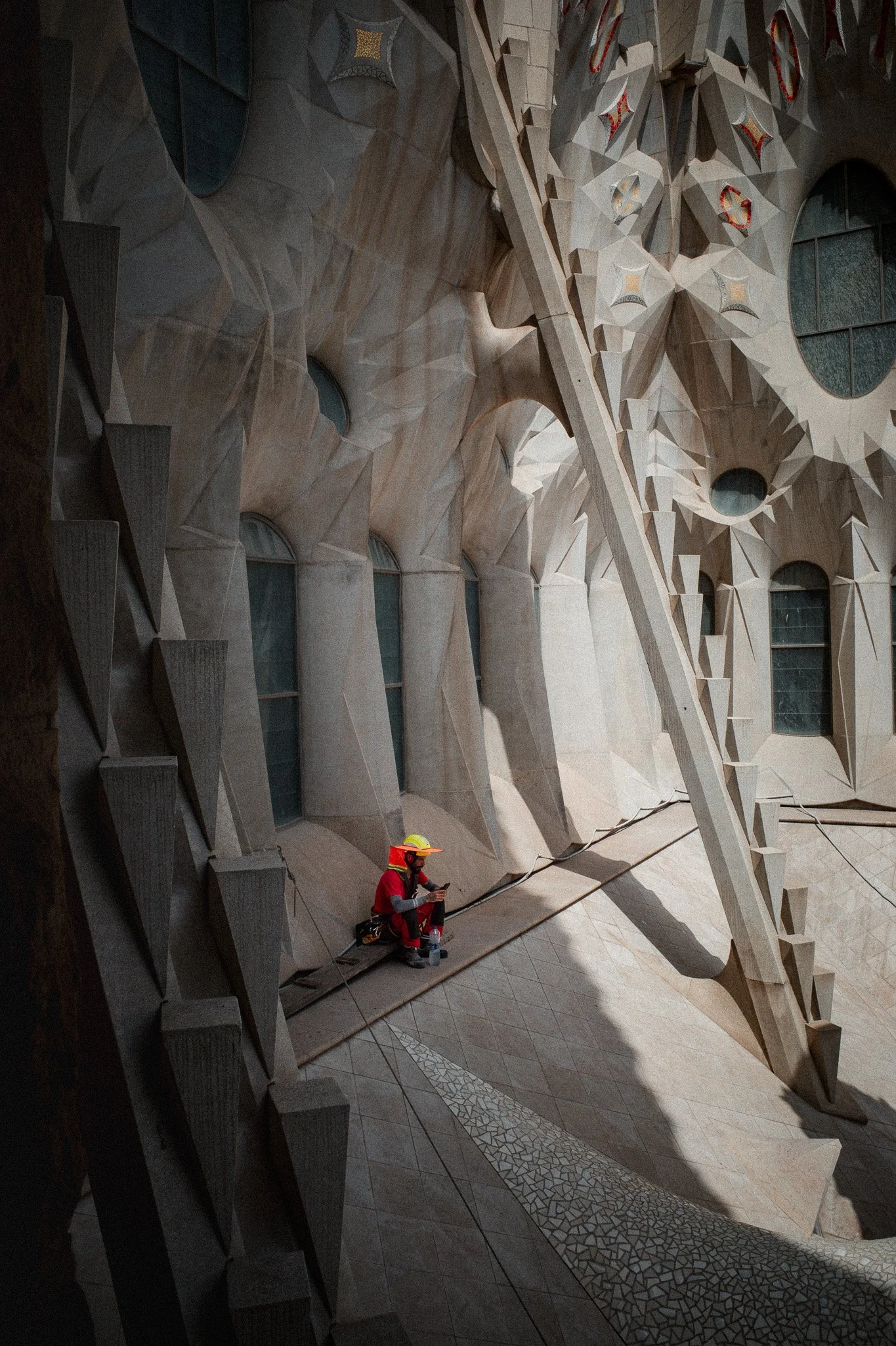 Un trabajador con casco y ropa de protección descansa sentado entre los andamios de las obras de la Sagrada Familia, con la luz entrando entre las columnas.