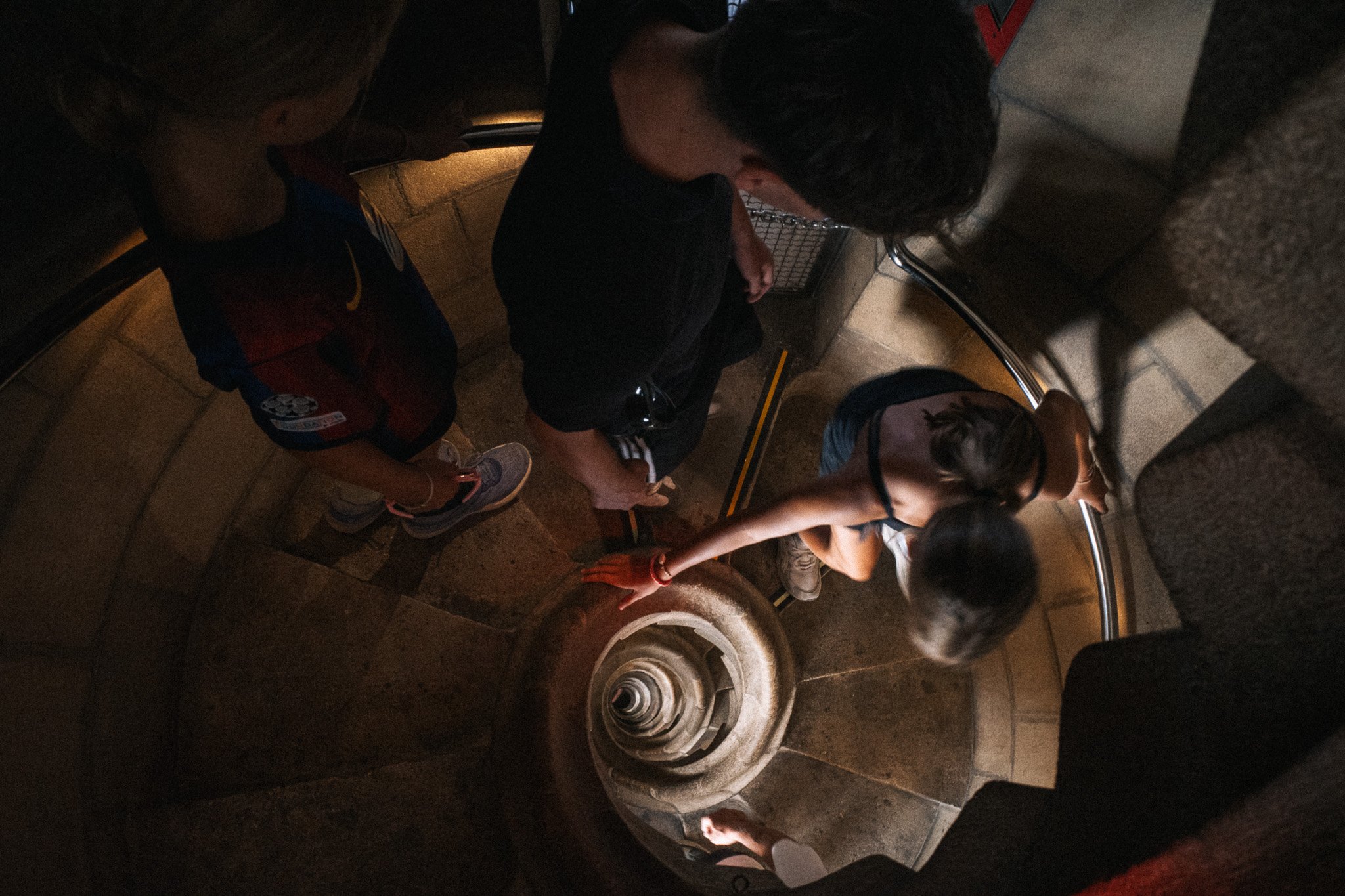 Vista cenital de una escalera de caracol de piedra en el interior de la Sagrada Familia, con varias personas bajando los escalones.