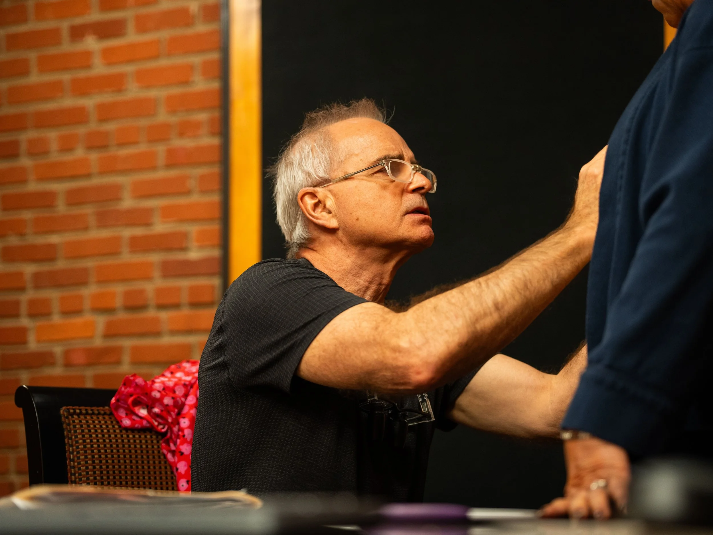 Dr. Chariker engaged in an intense conversation with a standing person in a blue shirt, with a brick wall and blackboard in the background.
