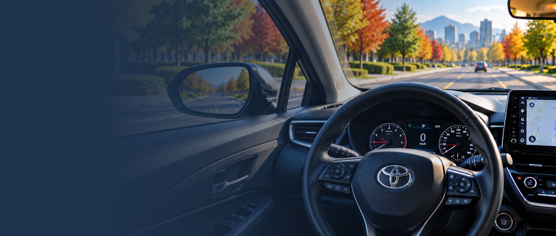 Inside a car, view of the dashboard and steering wheel, with a scenic autumn street seen through the windshield and side mirror, featuring trees with colorful fall foliage and mountains in the distance.