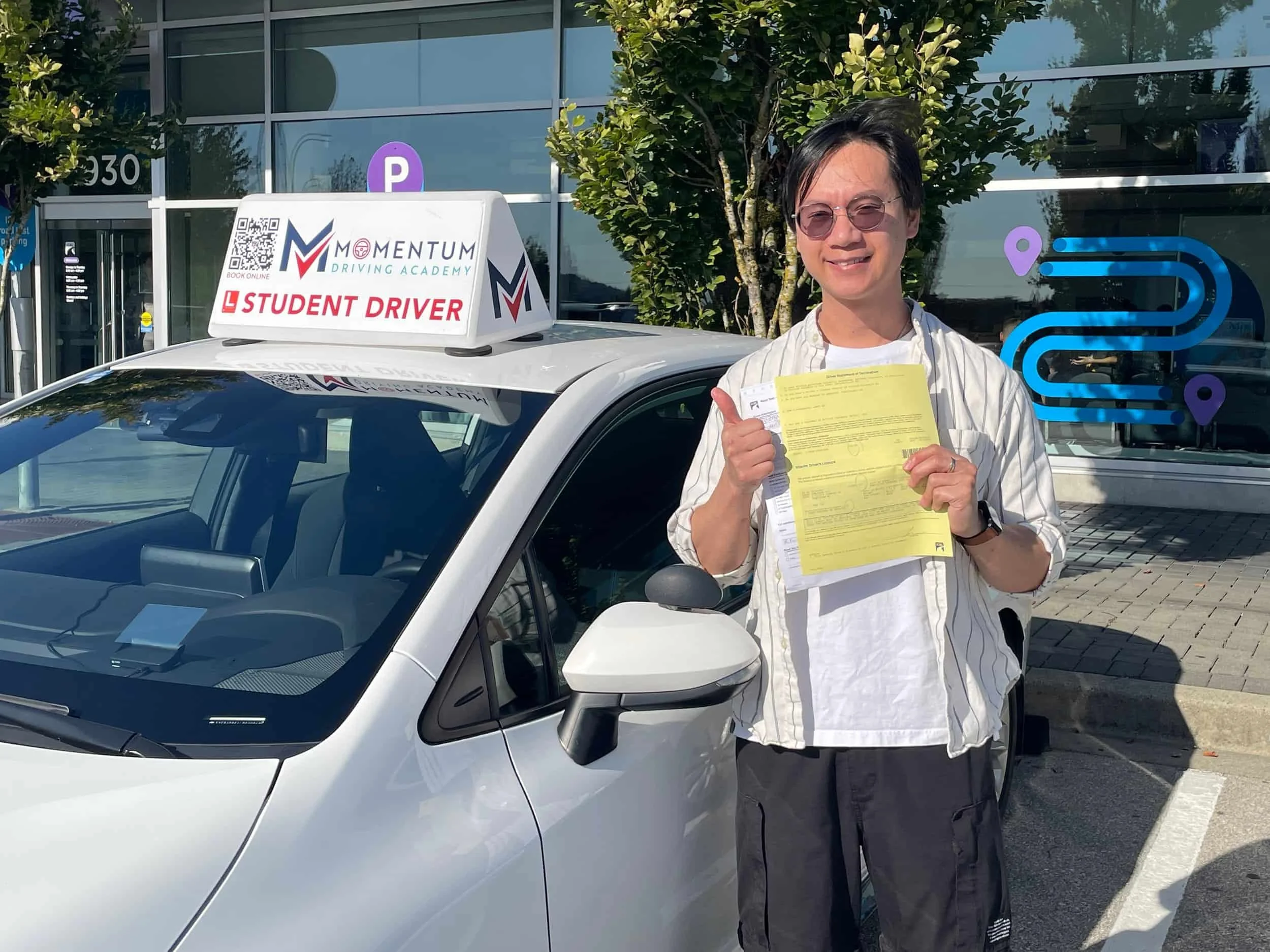 Smiling person stands by a car with a Student Driver sign, holding paperwork and giving a thumbs up outside a driving school.