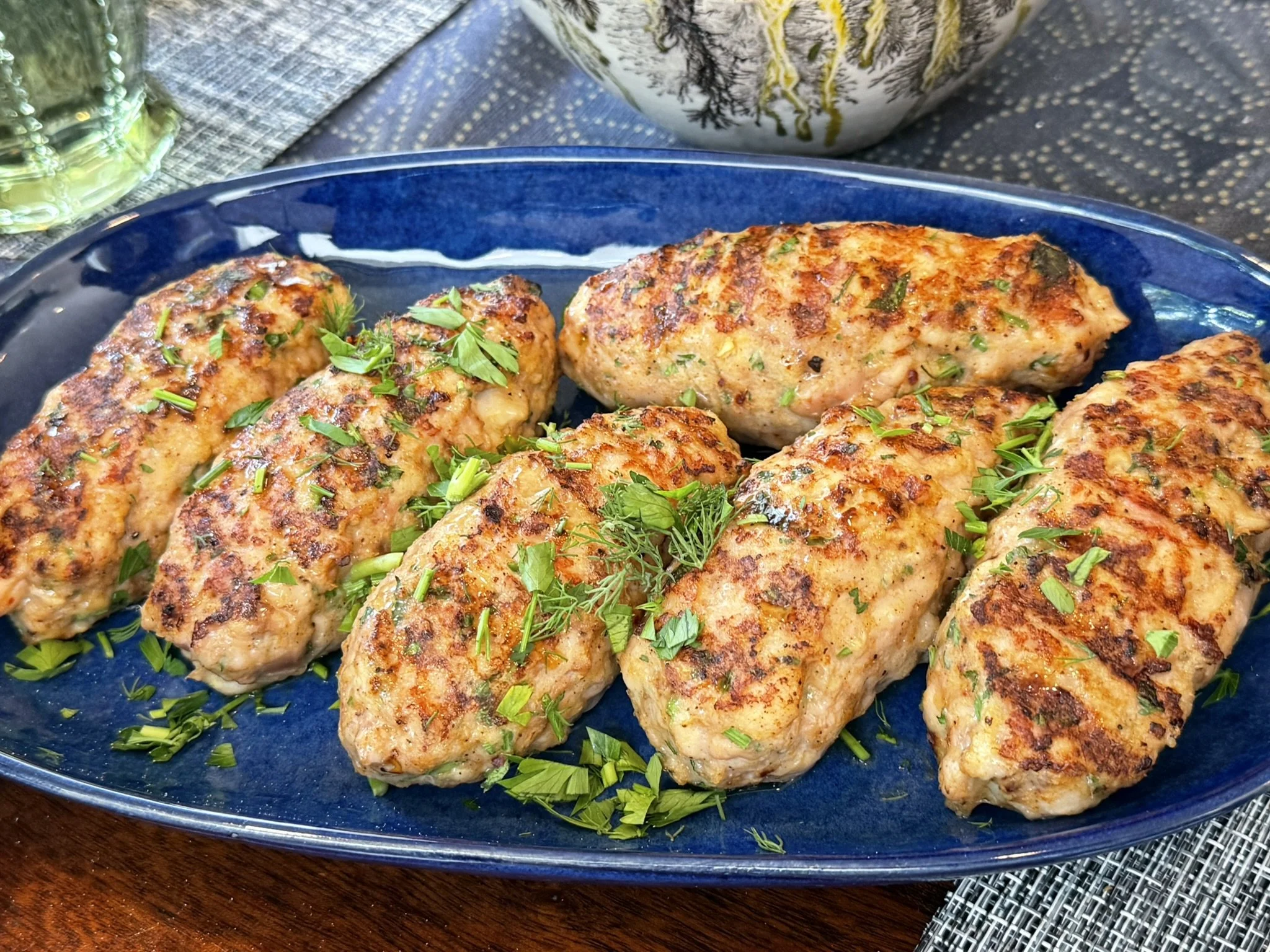 Close-up of chicken kofte patties garnished with chopped herbs on a blue ceramic plate.
